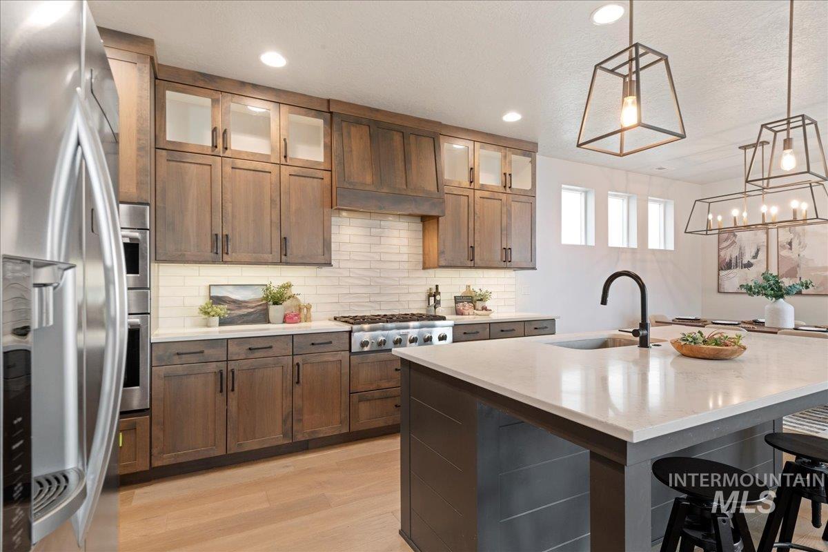 Kitchen featuring appliances with stainless steel finishes, tasteful backsplash, a breakfast bar area, decorative light fixtures, and light wood-style flooring