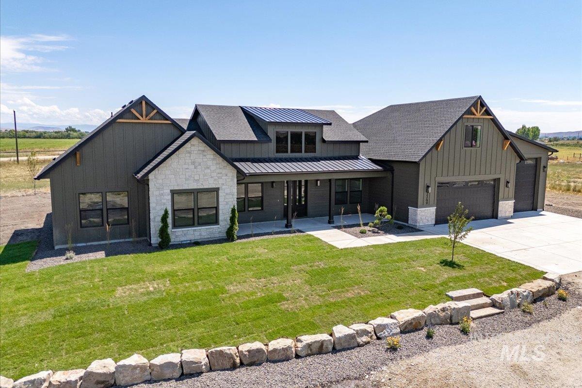 Modern inspired farmhouse featuring board and batten siding, stone siding, a standing seam roof, a metal roof, and driveway