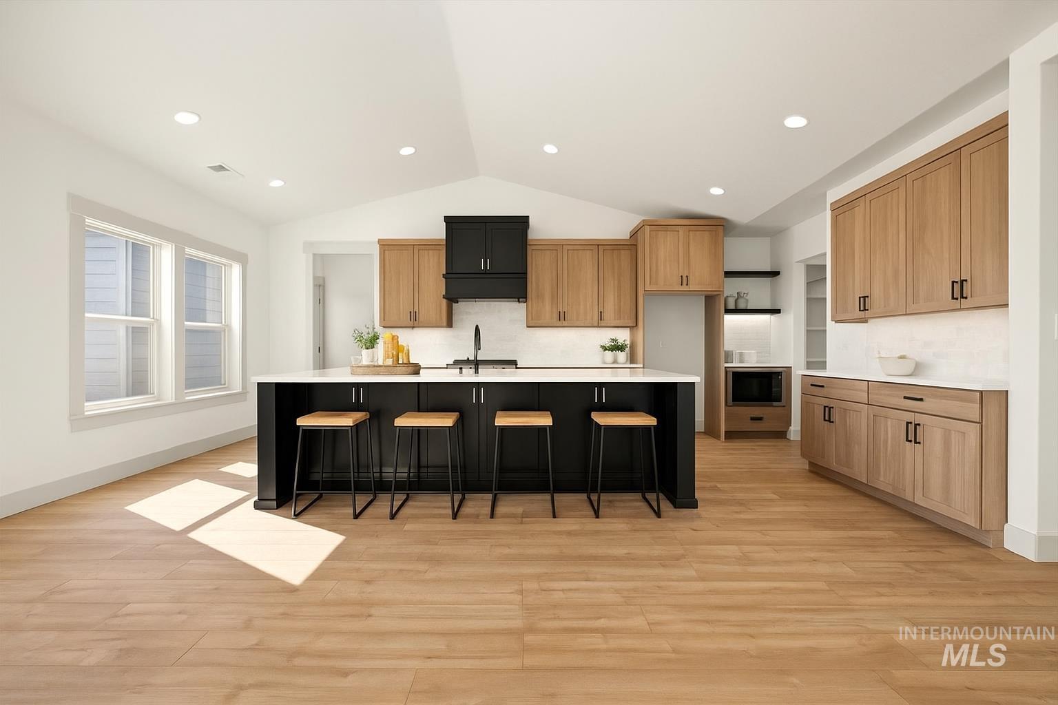 Kitchen with lofted ceiling, light countertops, tasteful backsplash, a center island with sink, and light wood finished floors