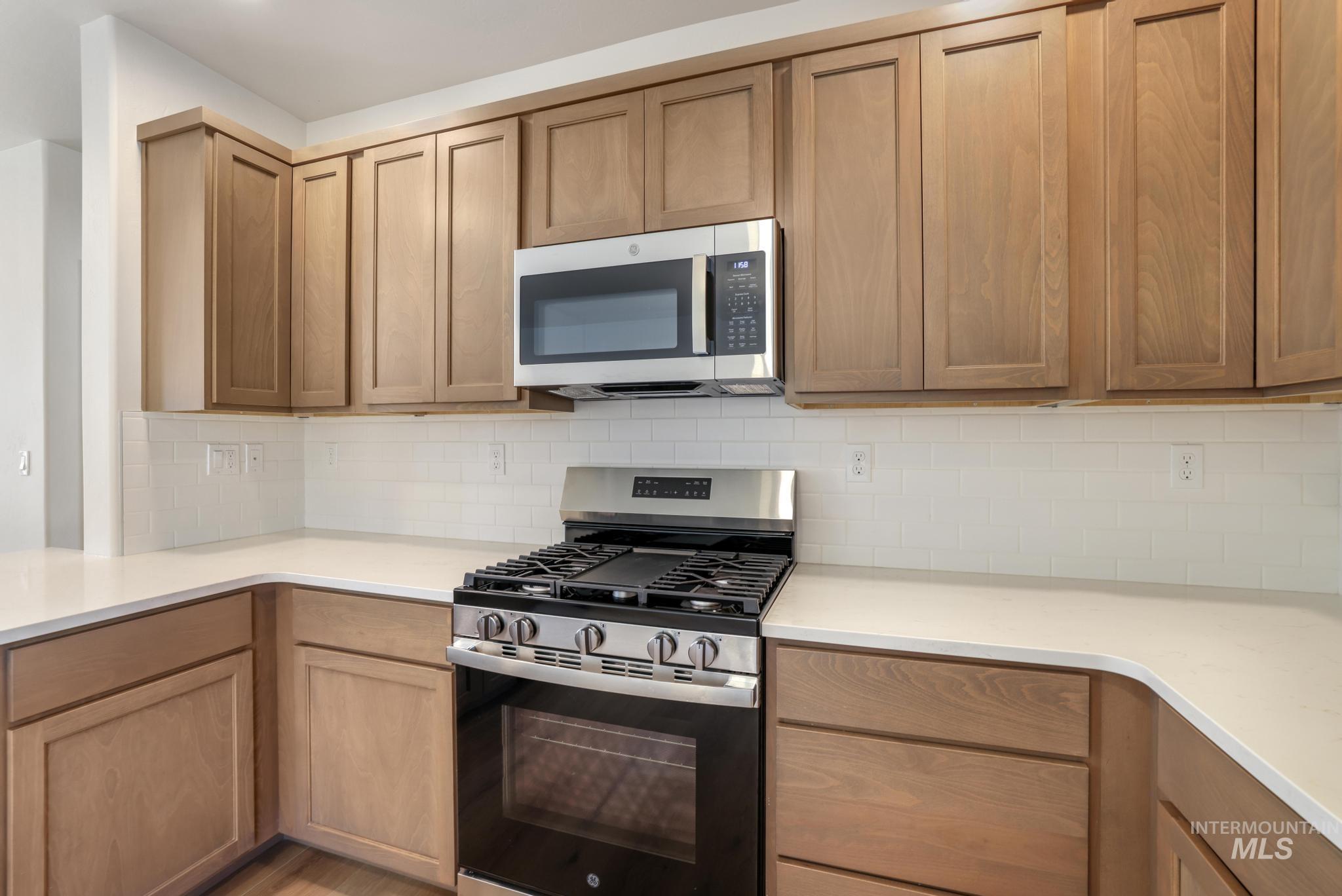 Kitchen featuring stainless steel appliances, decorative backsplash, and light stone countertops