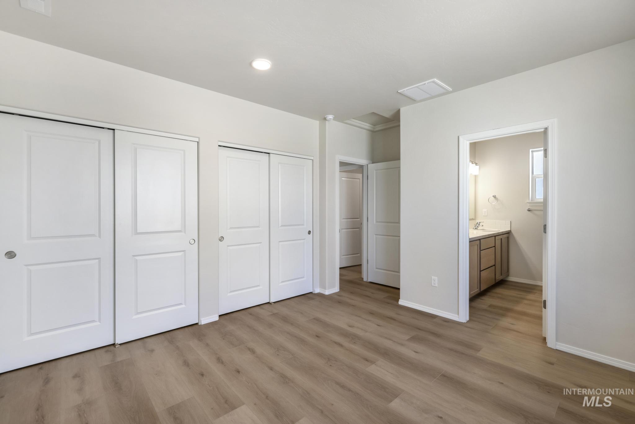 Unfurnished bedroom featuring light wood-type flooring, two closets, ensuite bath, and recessed lighting