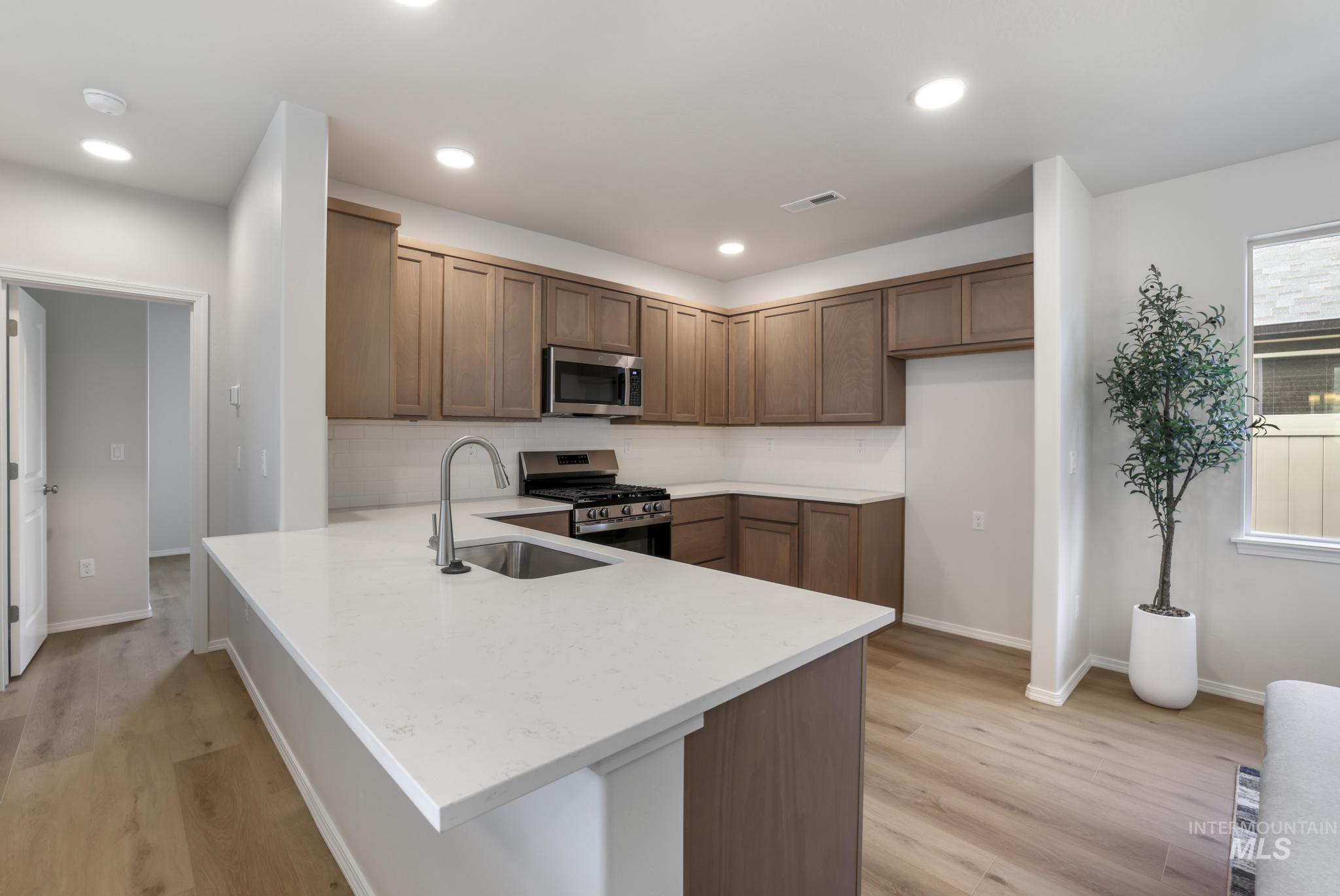 Kitchen with a peninsula, stainless steel appliances, light wood-type flooring, light stone countertops, and recessed lighting