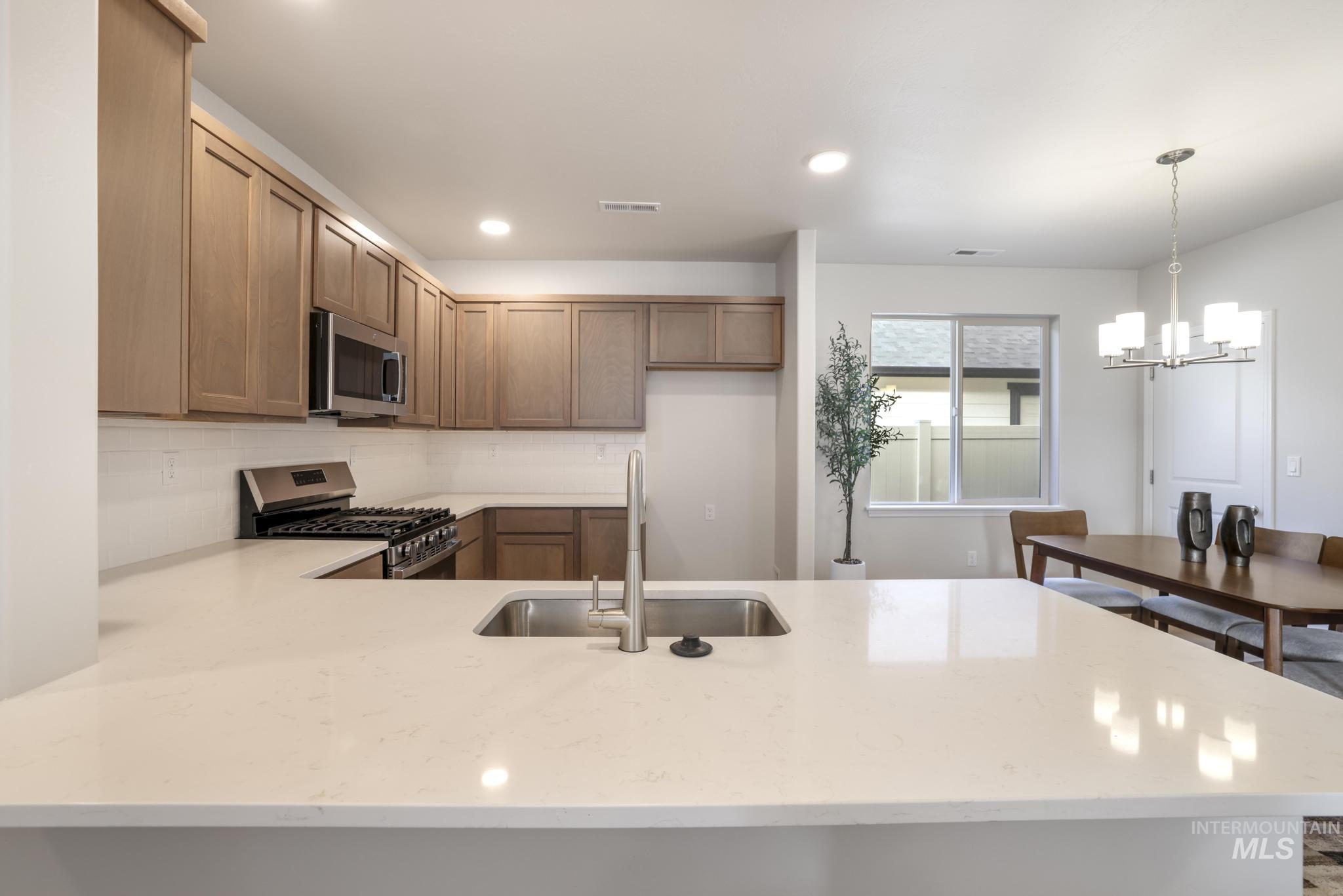 Kitchen with stainless steel appliances, a peninsula, hanging light fixtures, recessed lighting, and backsplash