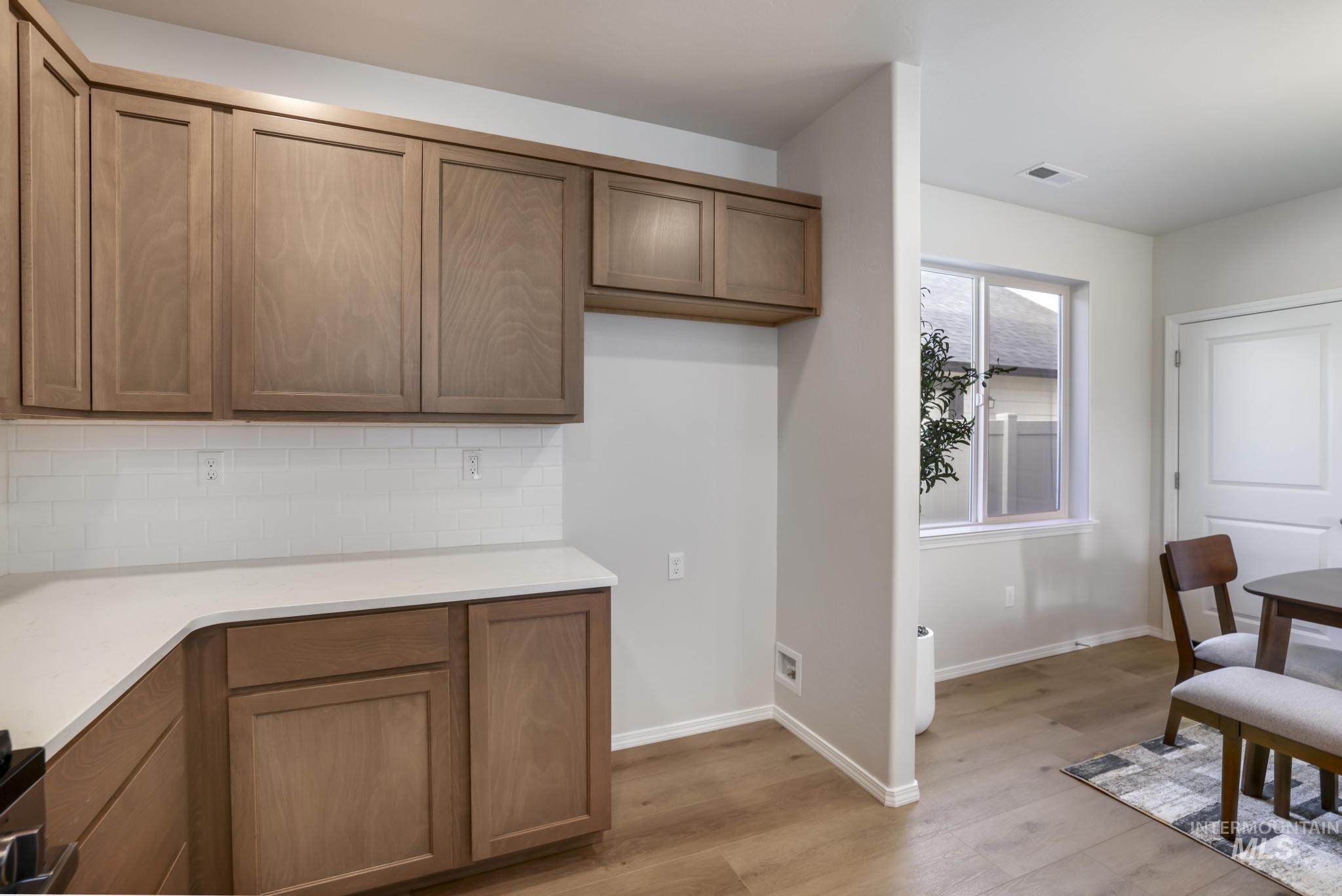 Kitchen featuring brown cabinetry, tasteful backsplash, light wood finished floors, and light stone counters