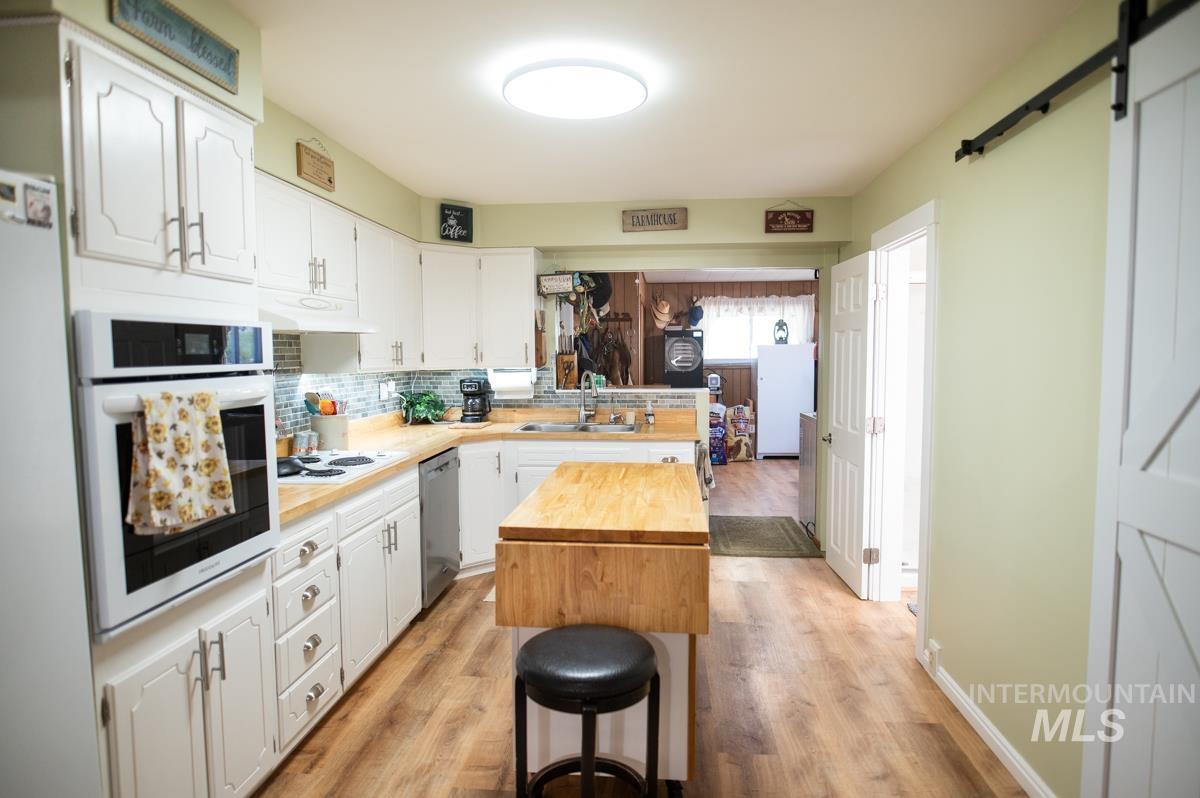 Kitchen featuring a barn door, wood counters, white cabinets, and white appliances