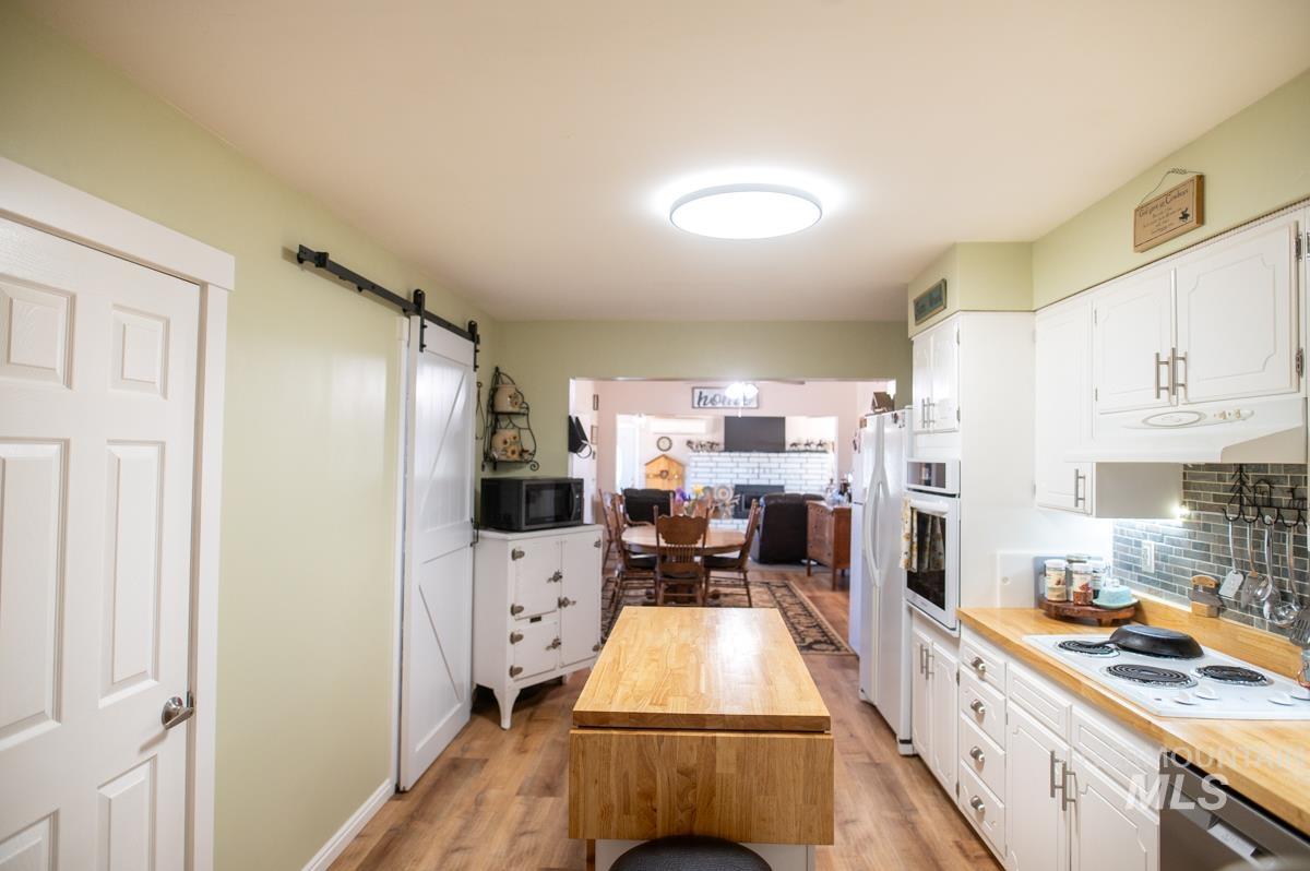 Kitchen with wooden counters, a barn door, decorative backsplash, white cabinetry, and light wood-style floors