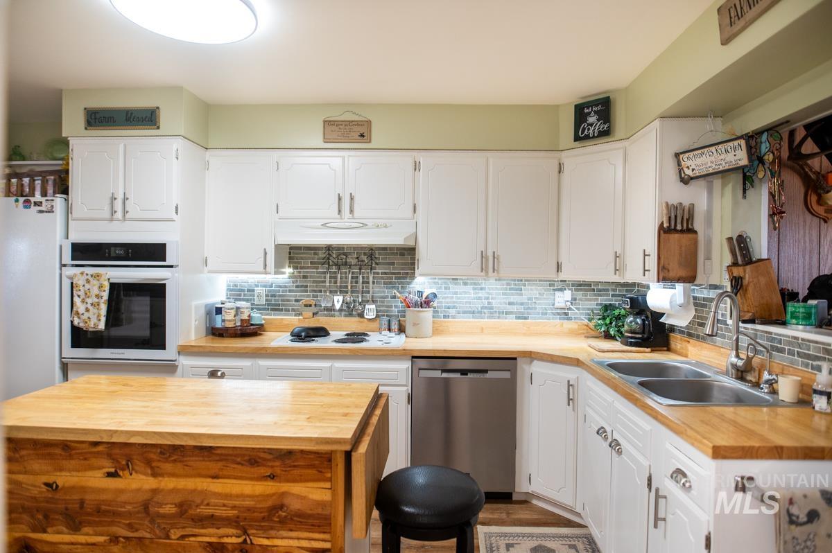 Kitchen with butcher block countertops, tasteful backsplash, white appliances, and white cabinetry