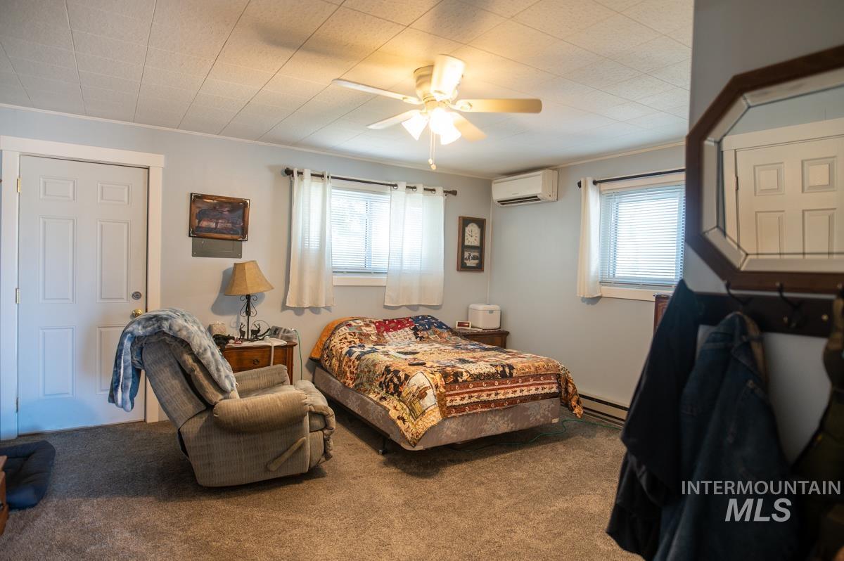 Carpeted bedroom featuring ceiling fan, ornamental molding, an AC wall unit, and a baseboard radiator