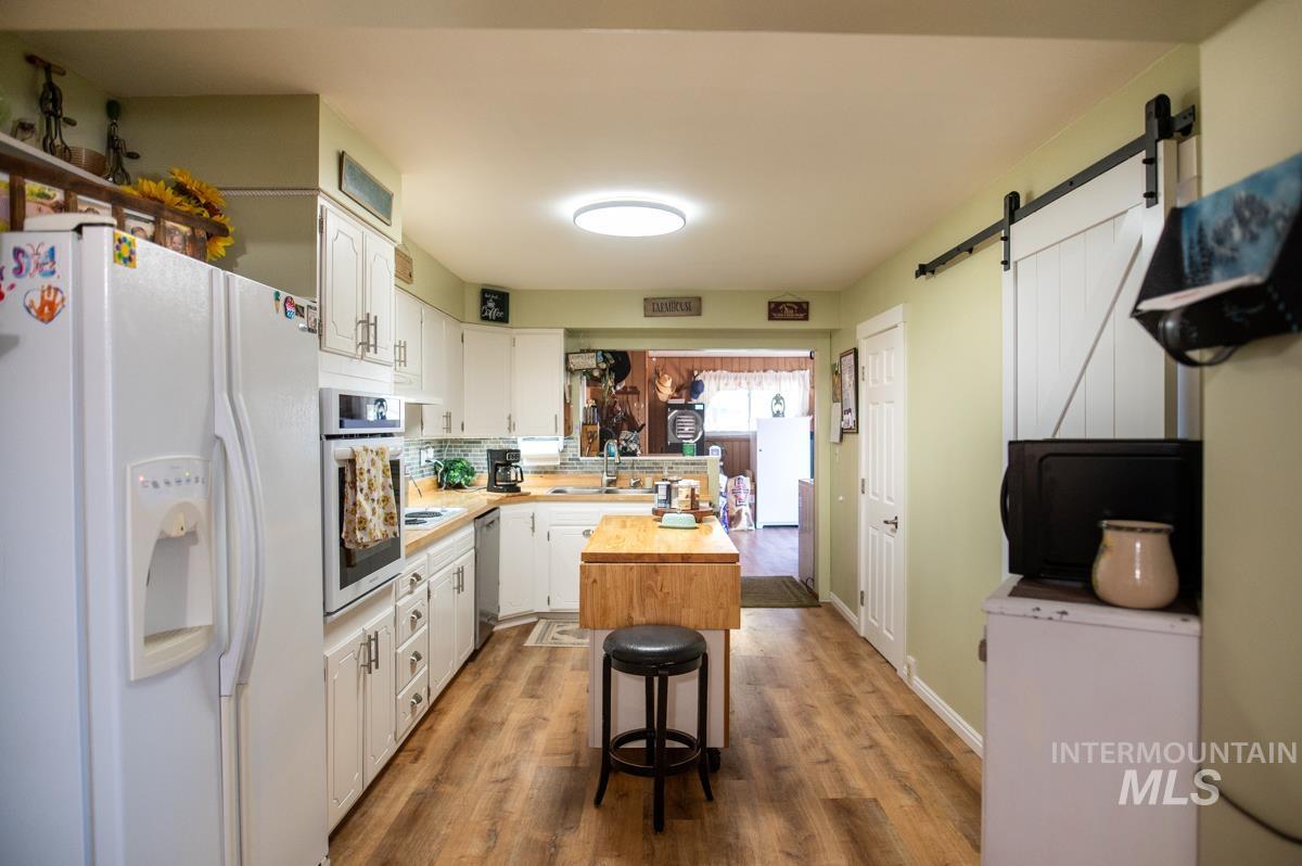 Kitchen with stainless steel appliances, white cabinetry, a barn door, and dark wood-style flooring