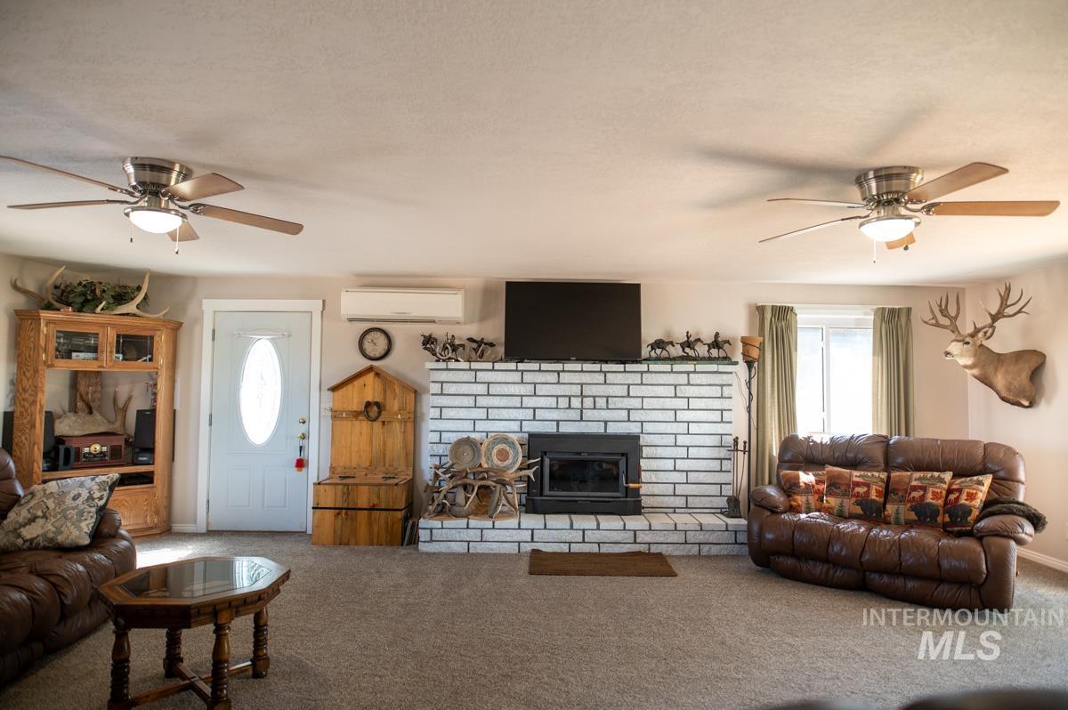Carpeted living room featuring a ceiling fan, a fireplace, and a wall mounted air conditioner