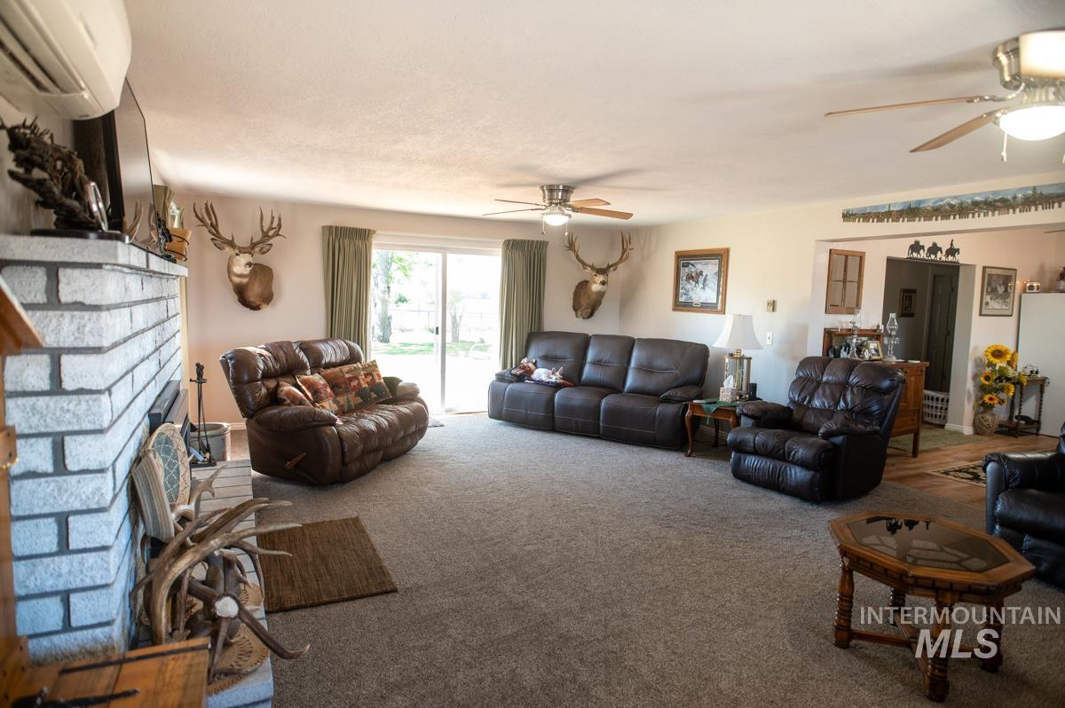 Living area with a wall unit AC, carpet floors, a fireplace, and ceiling fan