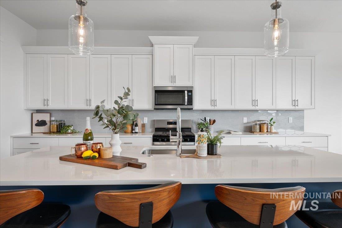 Kitchen featuring a kitchen bar, white cabinetry, stainless steel appliances, and decorative backsplash