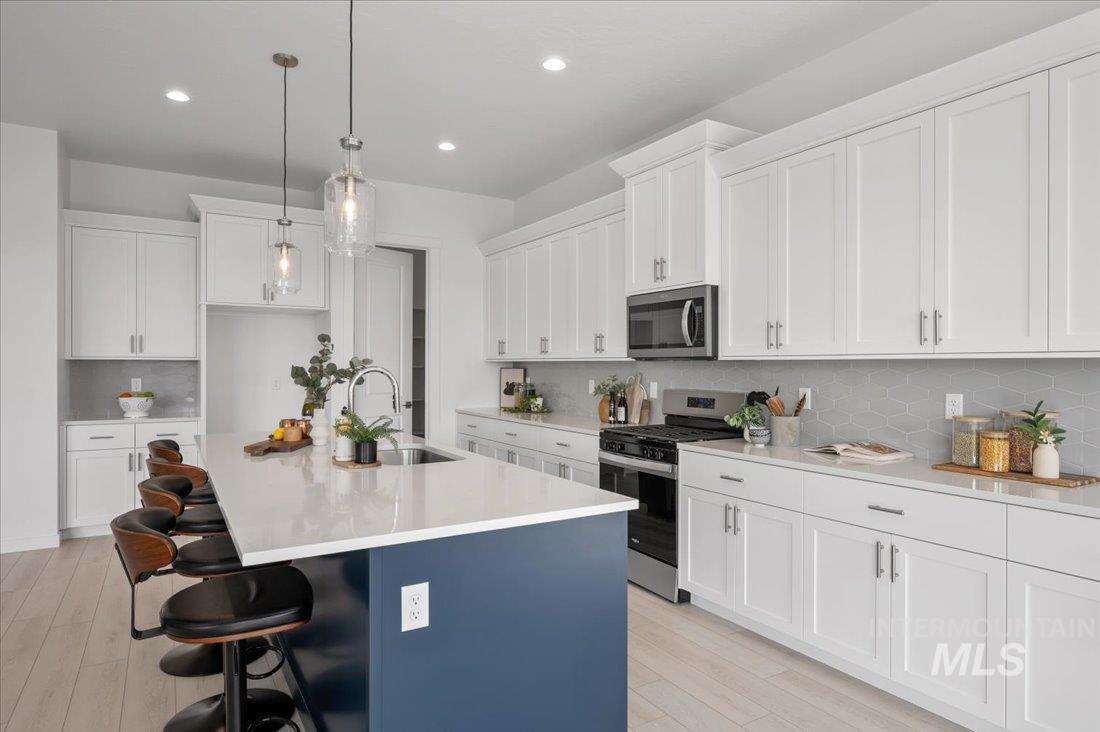 Kitchen with tasteful backsplash, appliances with stainless steel finishes, a kitchen breakfast bar, a center island with sink, and decorative light fixtures
