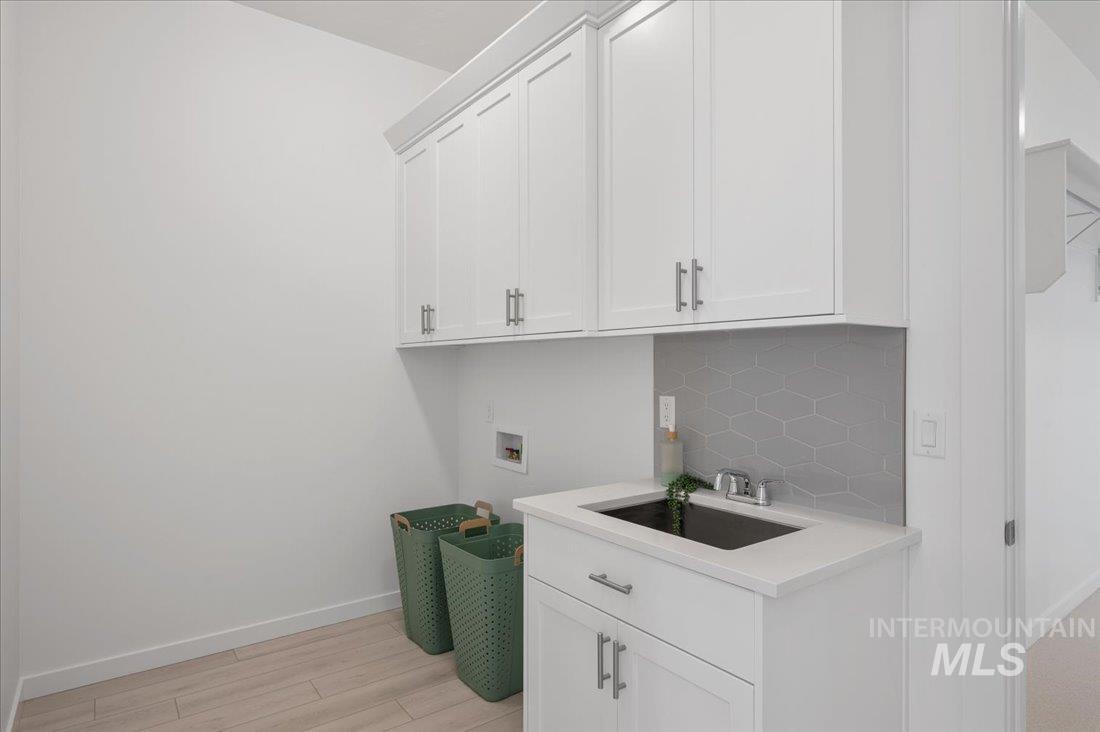 Laundry room with hookup for a washing machine, light wood finished floors, and cabinet space
