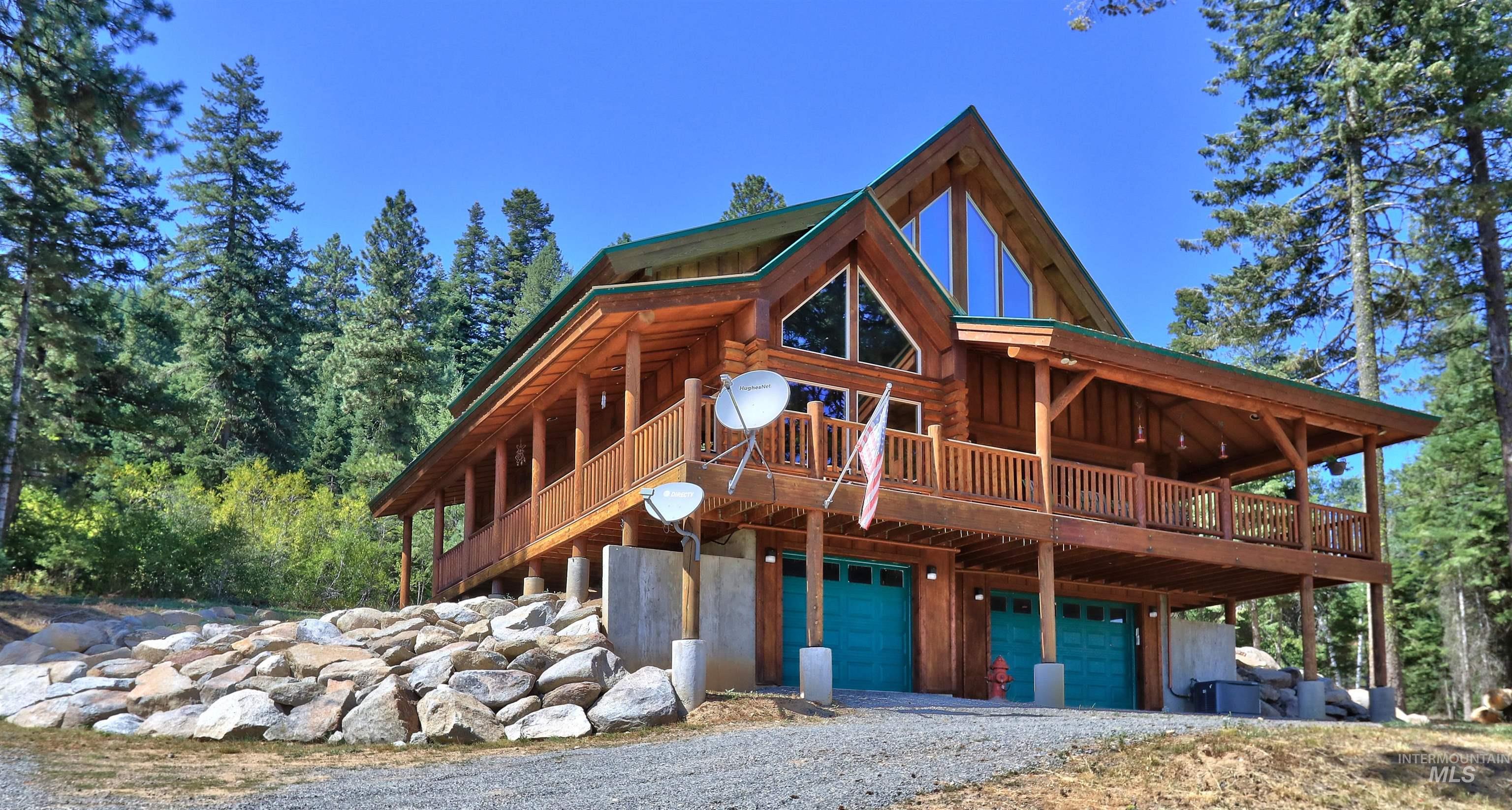 View of front of home featuring a wooden deck, an attached garage, gravel driveway, and log exterior