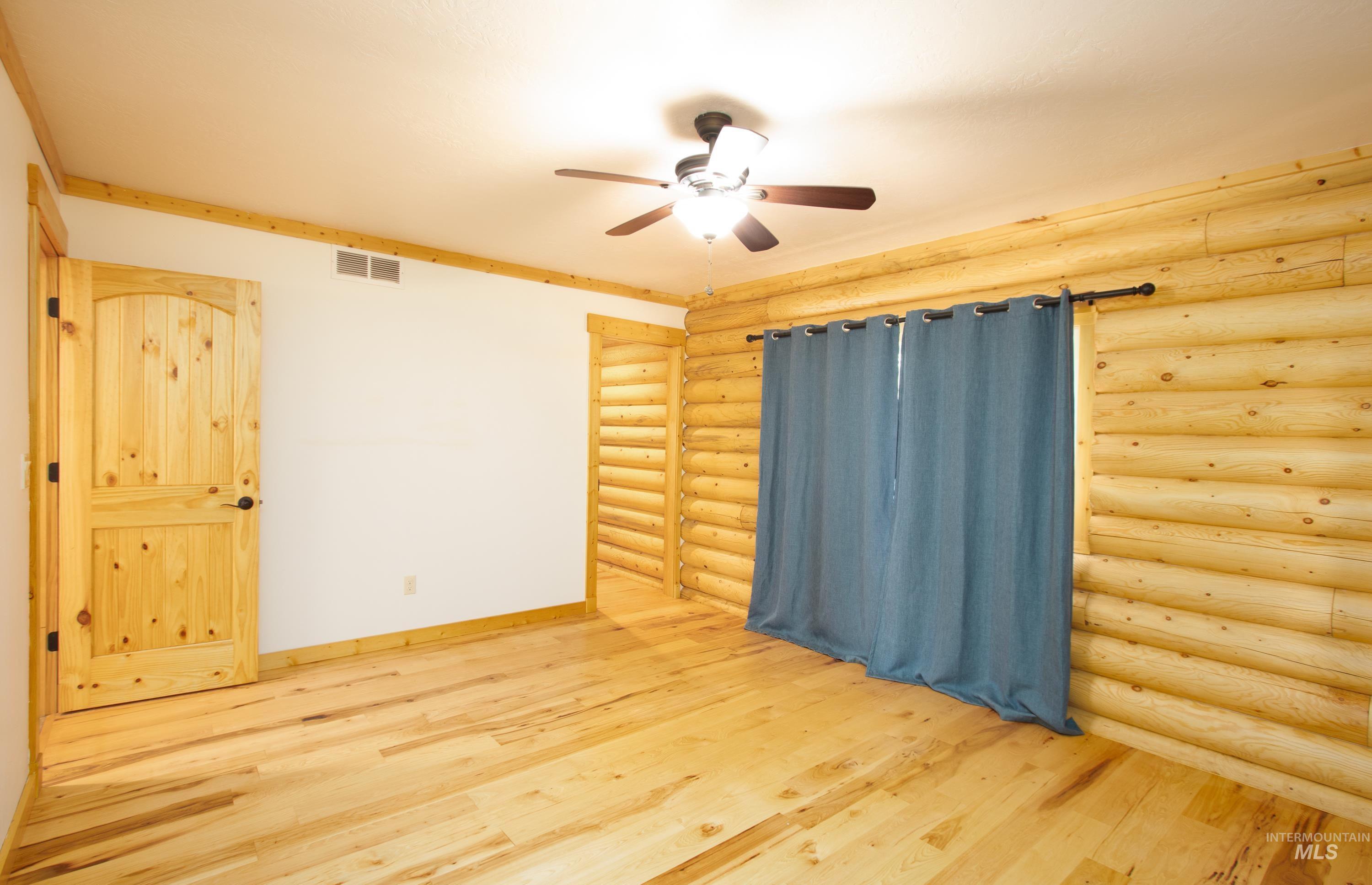 Empty room featuring log walls, light wood-style flooring, and a ceiling fan