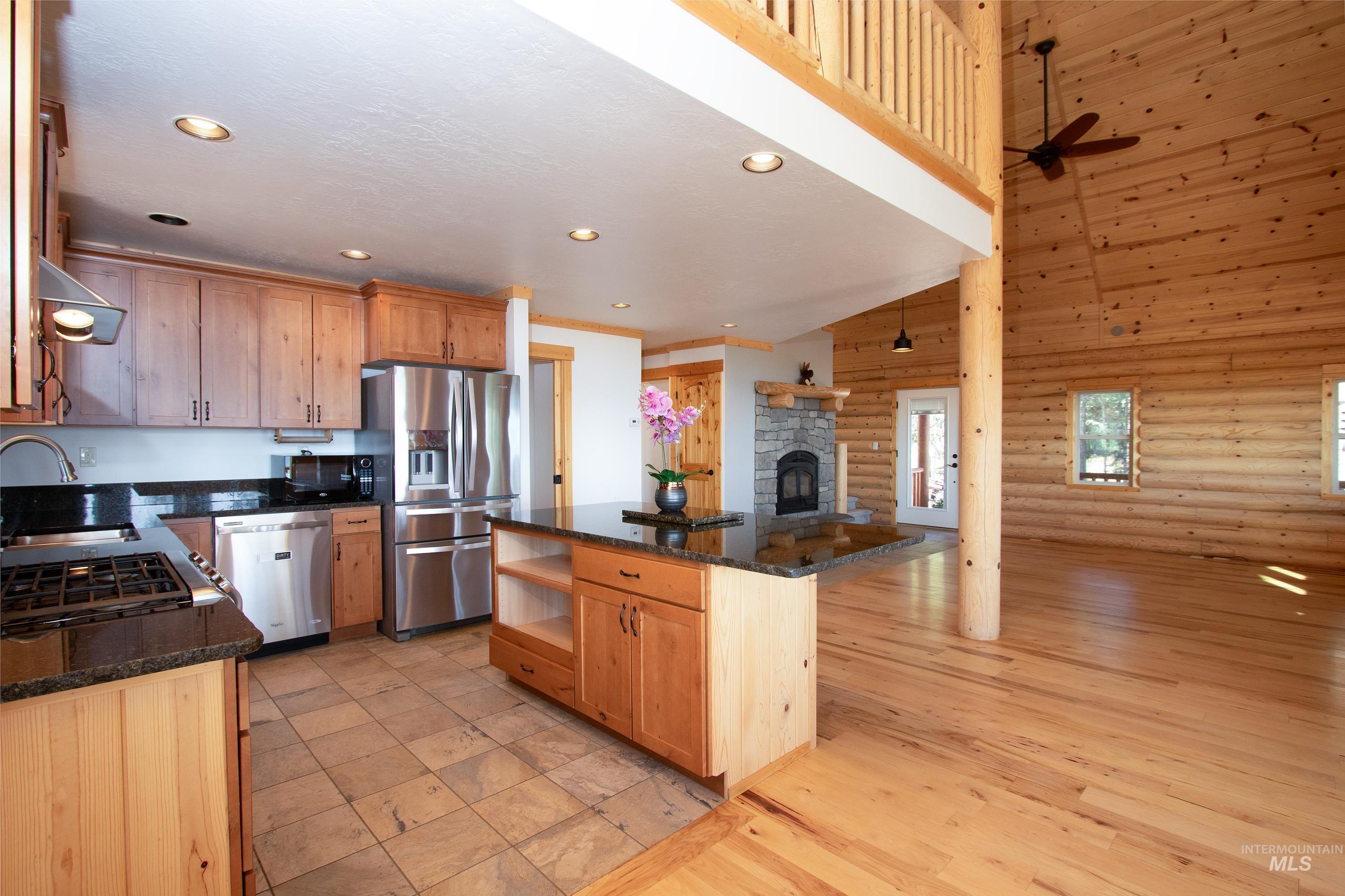 Kitchen with rustic walls, a kitchen island, stainless steel appliances, a stone fireplace, and range hood