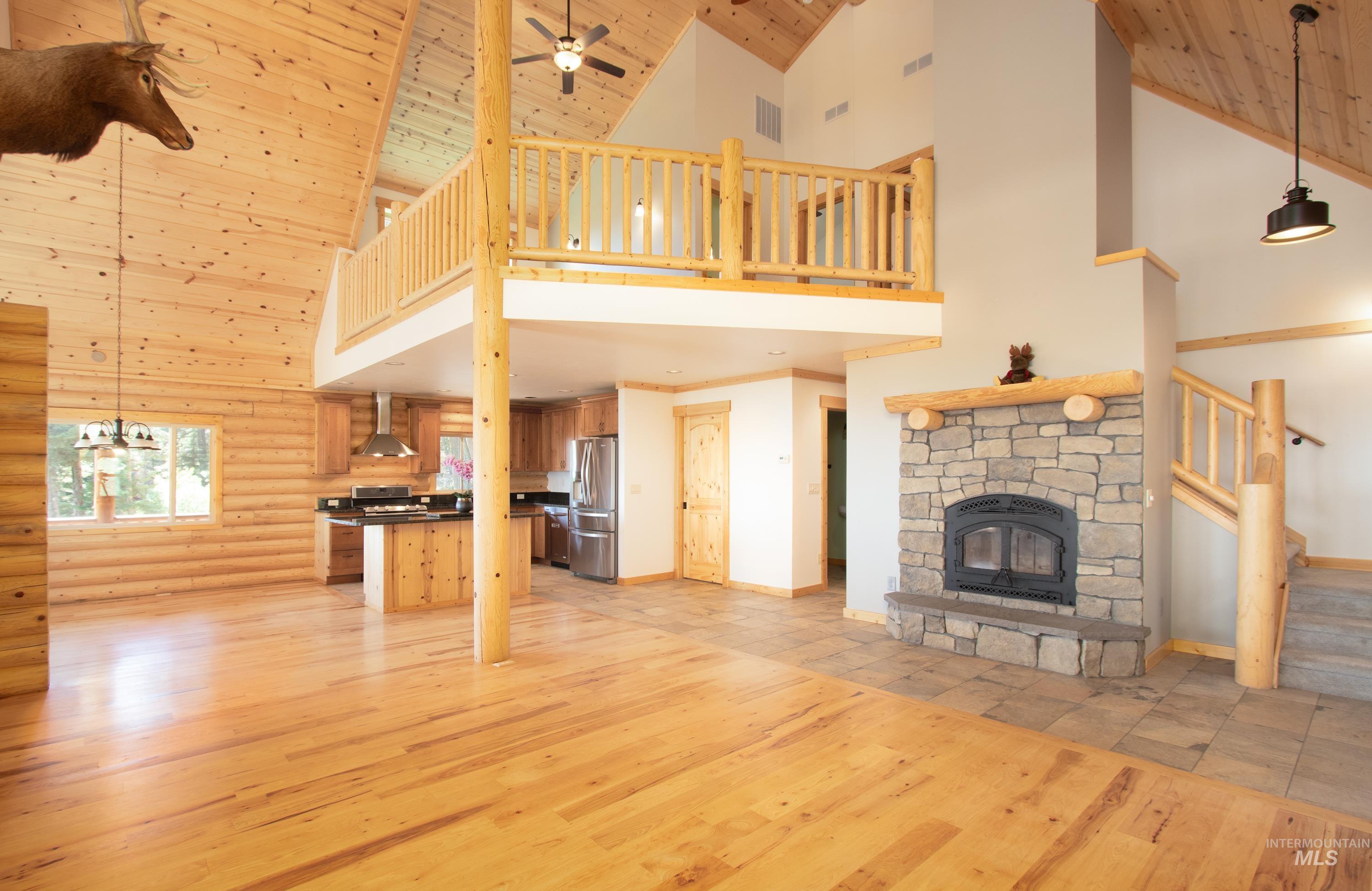 Unfurnished living room featuring light wood-style floors, rustic walls, a fireplace, a vaulted wood ceiling, and a ceiling fan