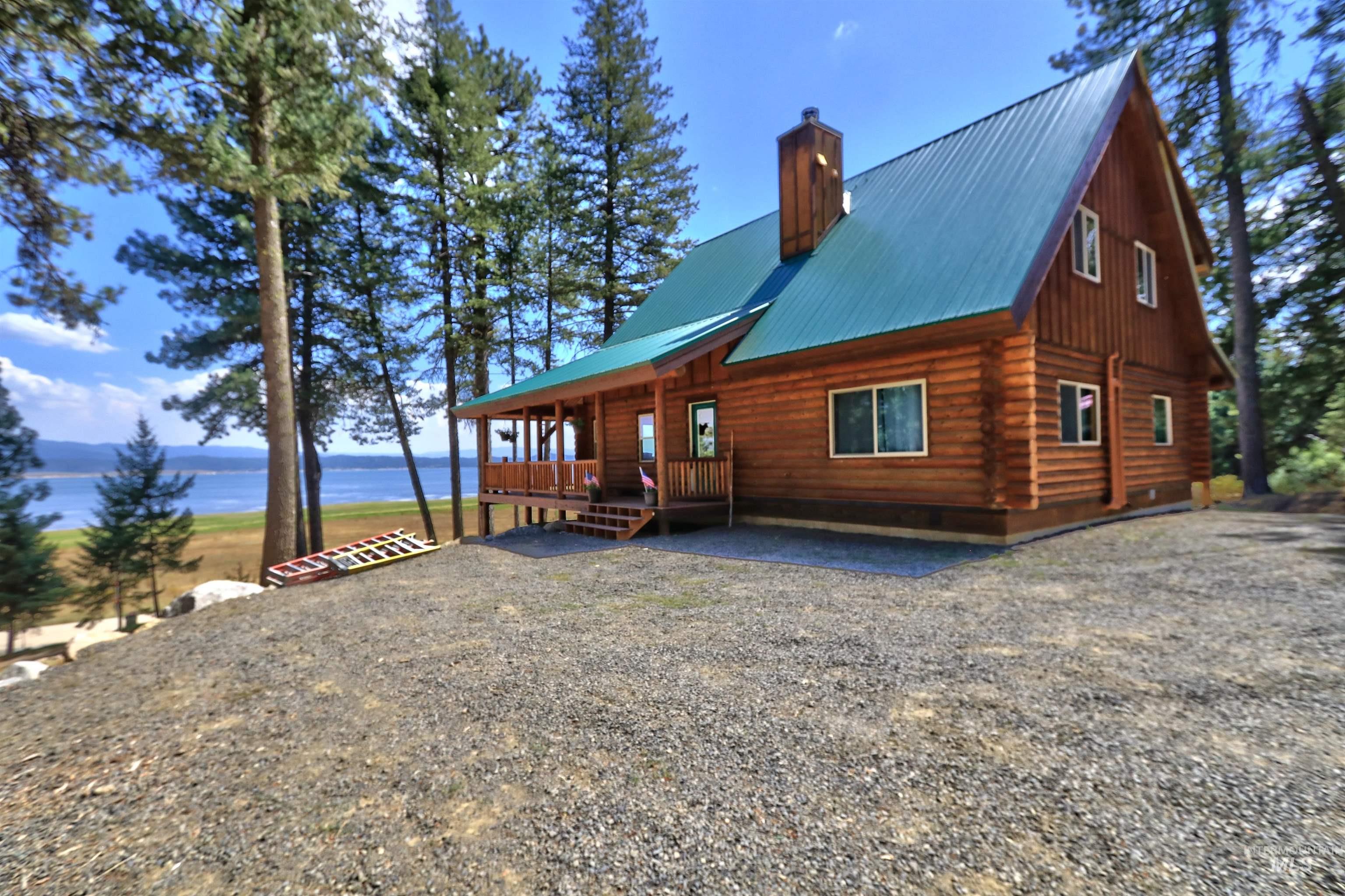 Back of house featuring a water view, covered porch, a metal roof, a chimney, and log siding