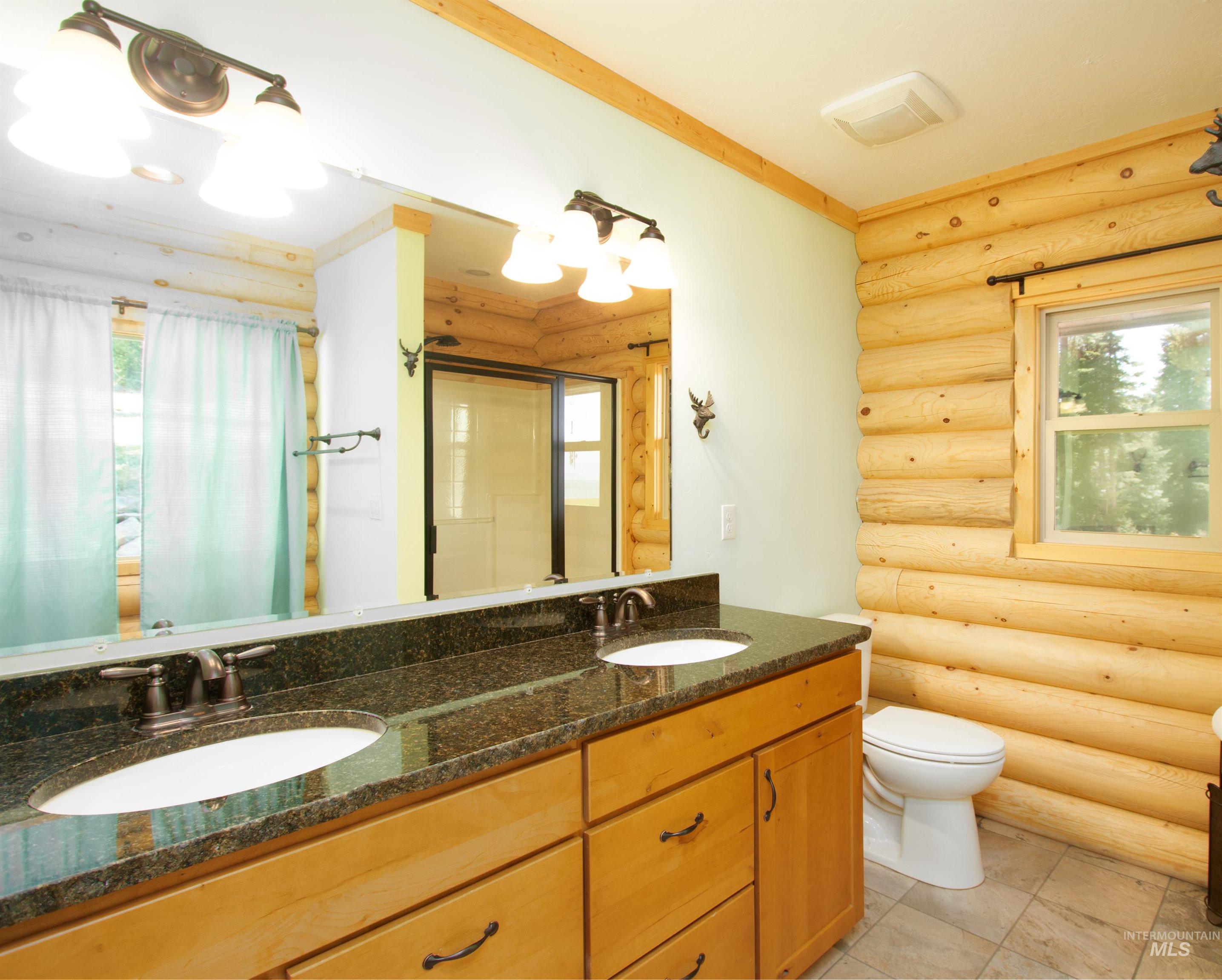 Bathroom with log walls, healthy amount of natural light, double vanity, crown molding, and a shower