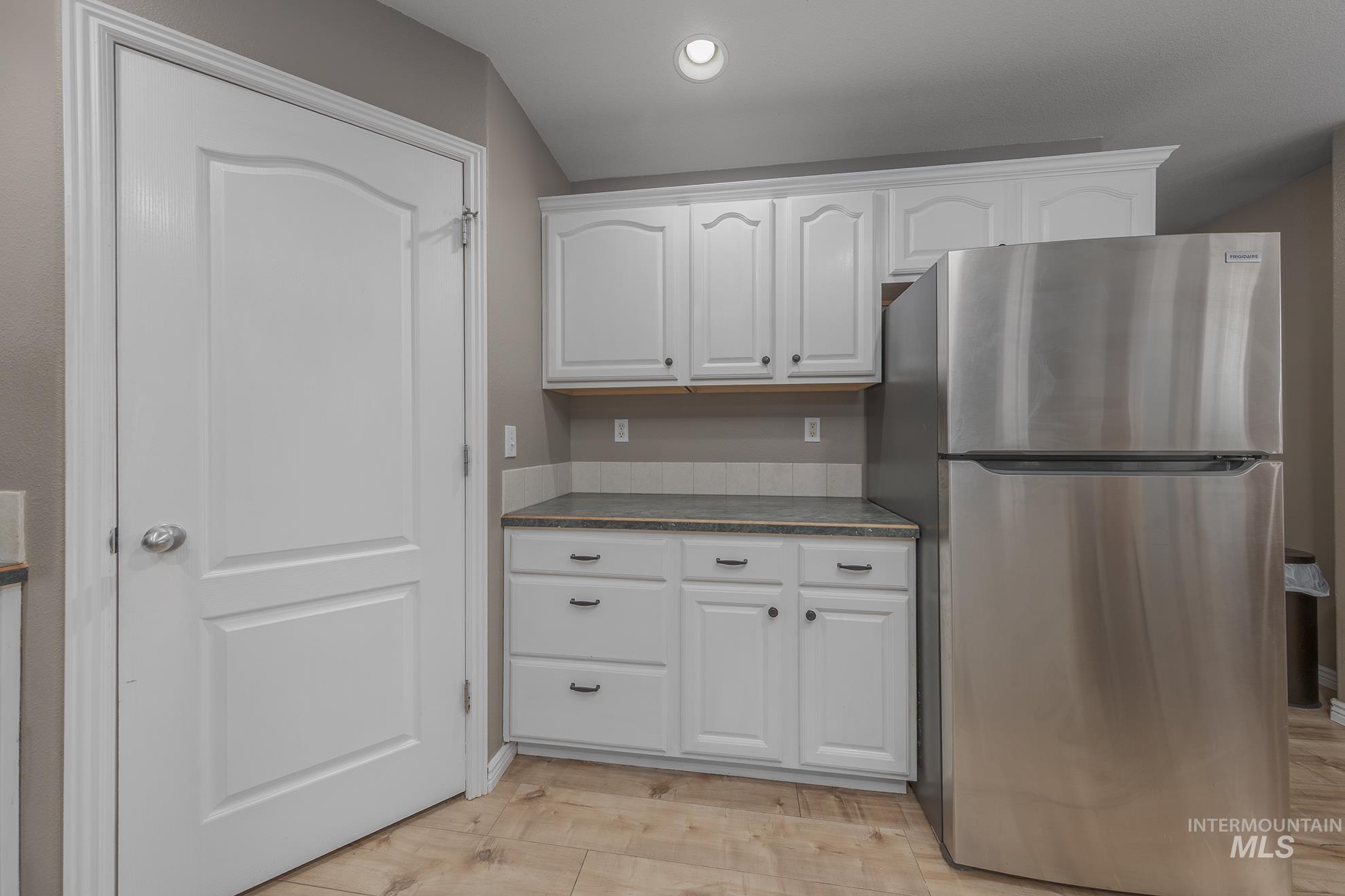 Kitchen featuring freestanding refrigerator, white cabinets, dark countertops, light wood-style flooring, and recessed lighting
