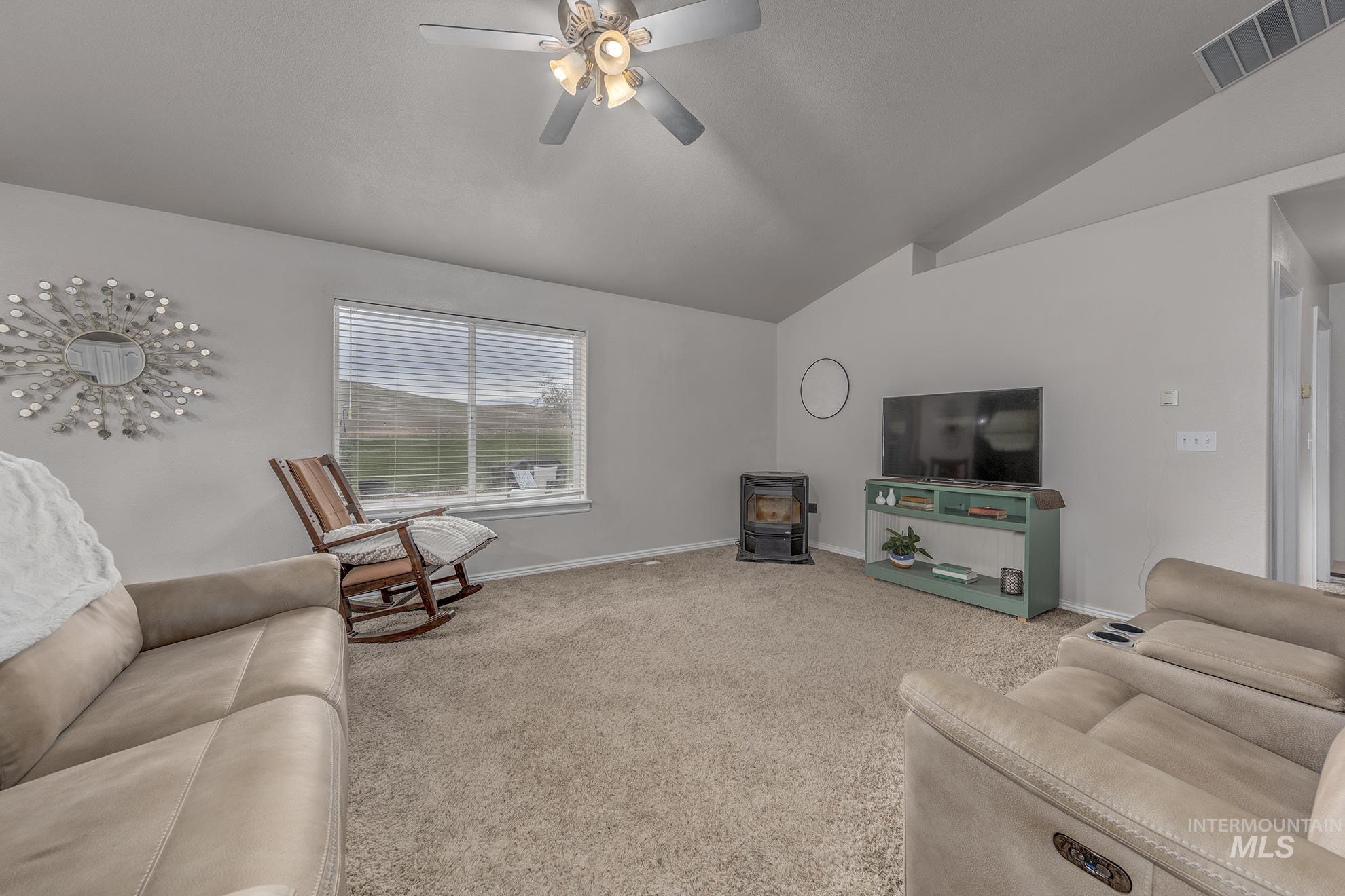 Living area featuring a wood stove, light colored carpet, lofted ceiling, and a ceiling fan