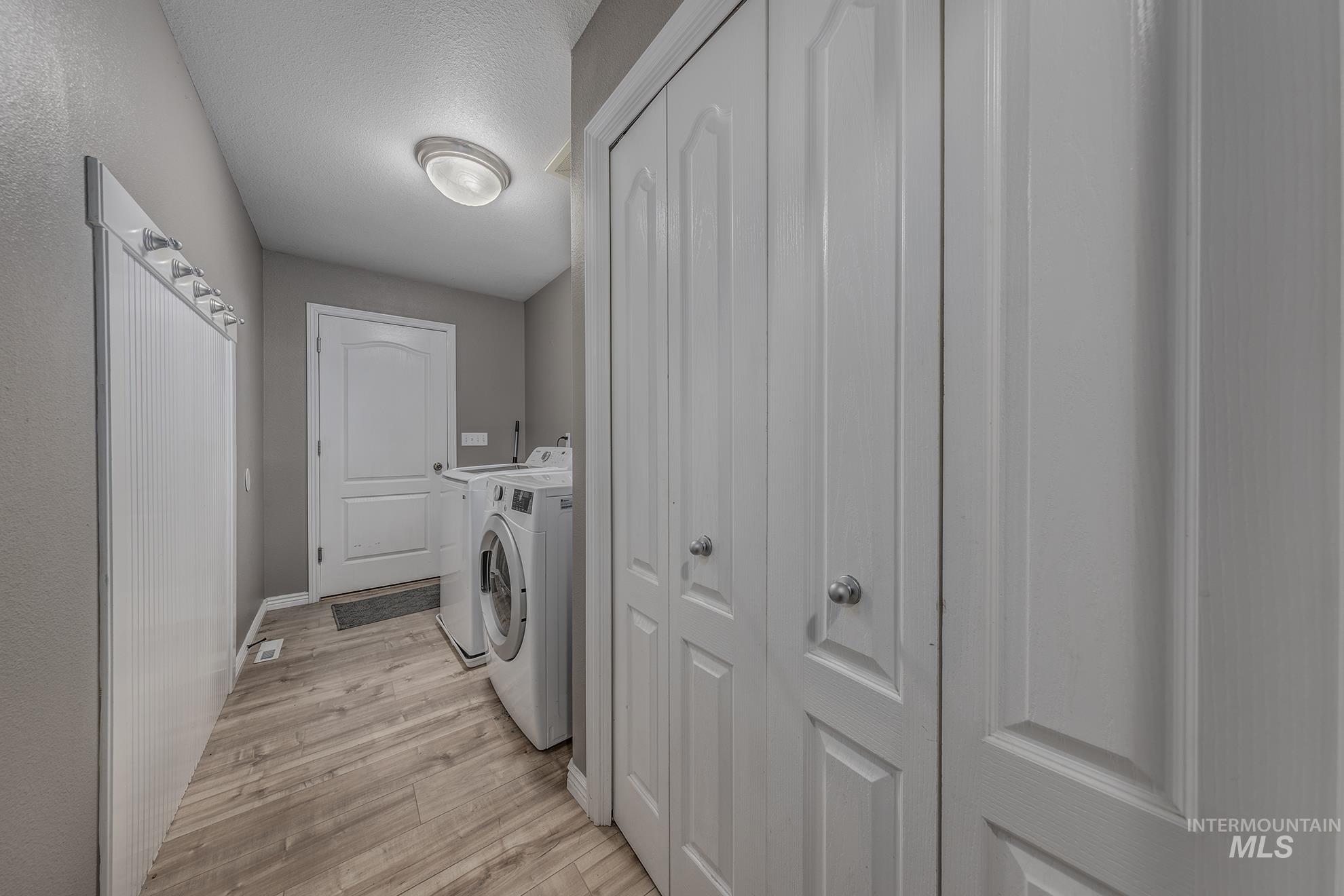 Laundry room with washing machine and dryer, light wood finished floors, and a textured ceiling