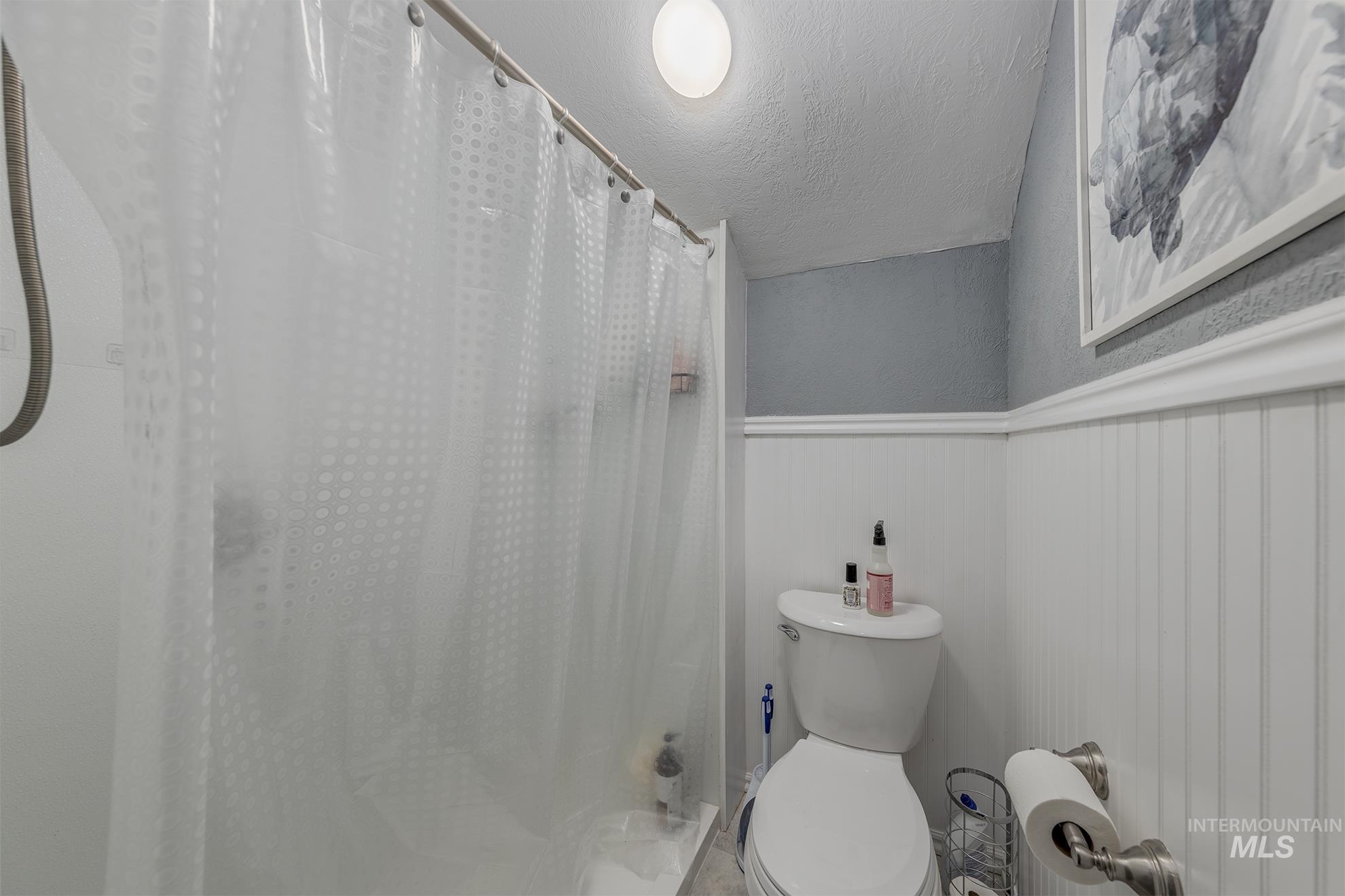 Bathroom with curtained shower, a textured ceiling, a textured wall, and wainscoting
