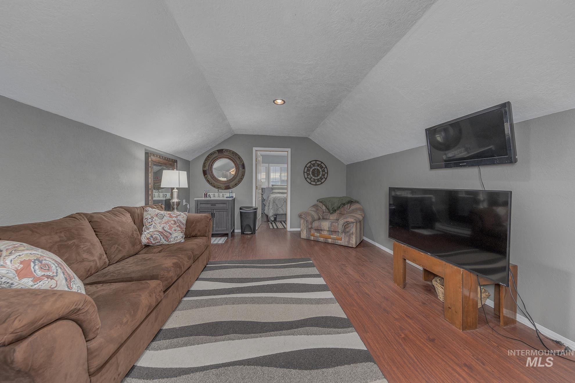 Living area with a textured ceiling, dark wood-type flooring, and vaulted ceiling