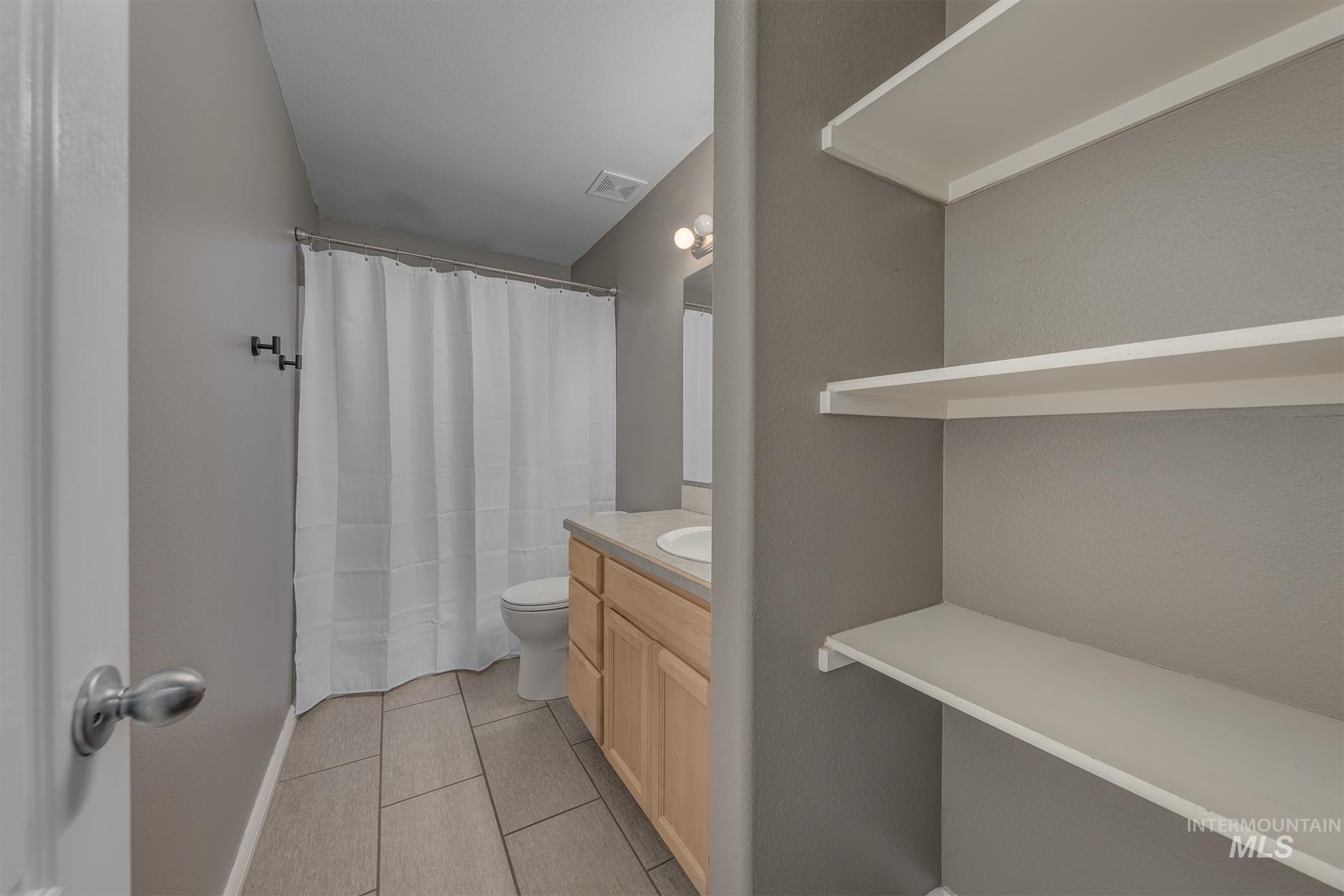 Full bathroom featuring vanity, light tile patterned flooring, and curtained shower