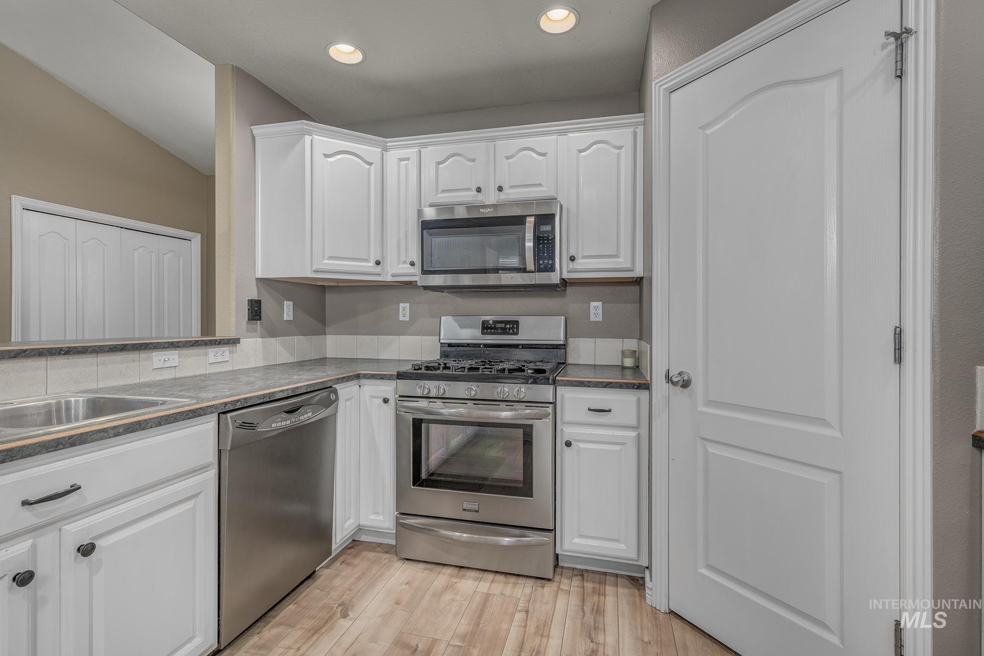 Kitchen with stainless steel appliances, white cabinetry, light wood finished floors, recessed lighting, and dark stone countertops