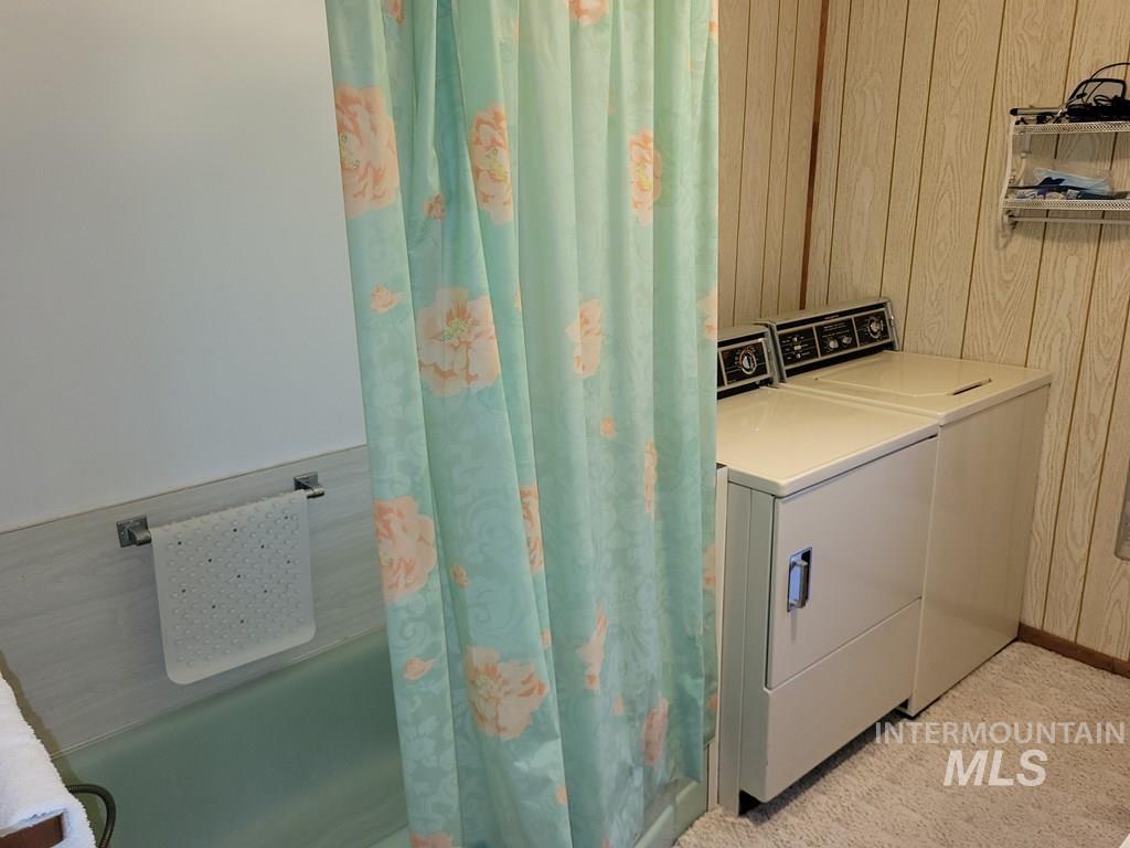 Laundry area with washer and dryer, wooden walls, and light carpet