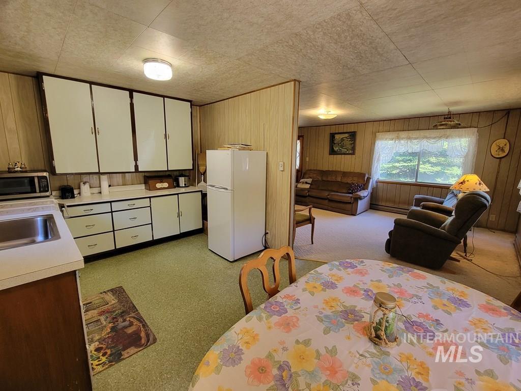 Kitchen with freestanding refrigerator, light countertops, stainless steel microwave, wooden walls, and white cabinetry