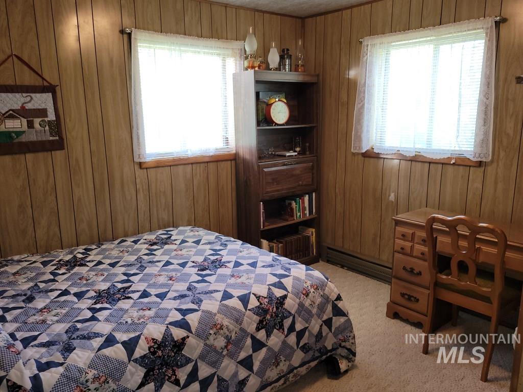 Bedroom featuring wooden walls, a baseboard heating unit, and light colored carpet