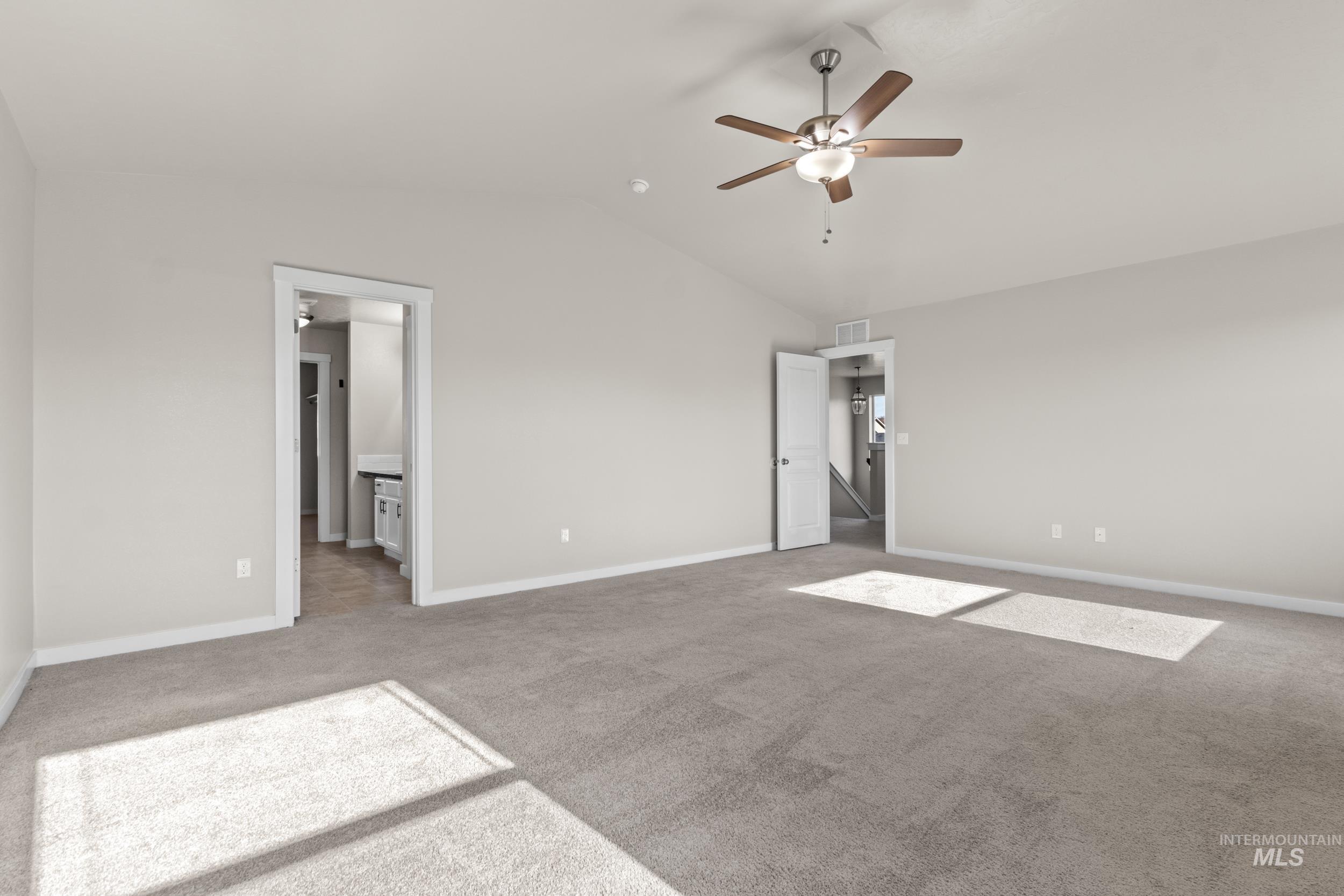 Unfurnished bedroom featuring light colored carpet, lofted ceiling, ceiling fan, and ensuite bathroom
