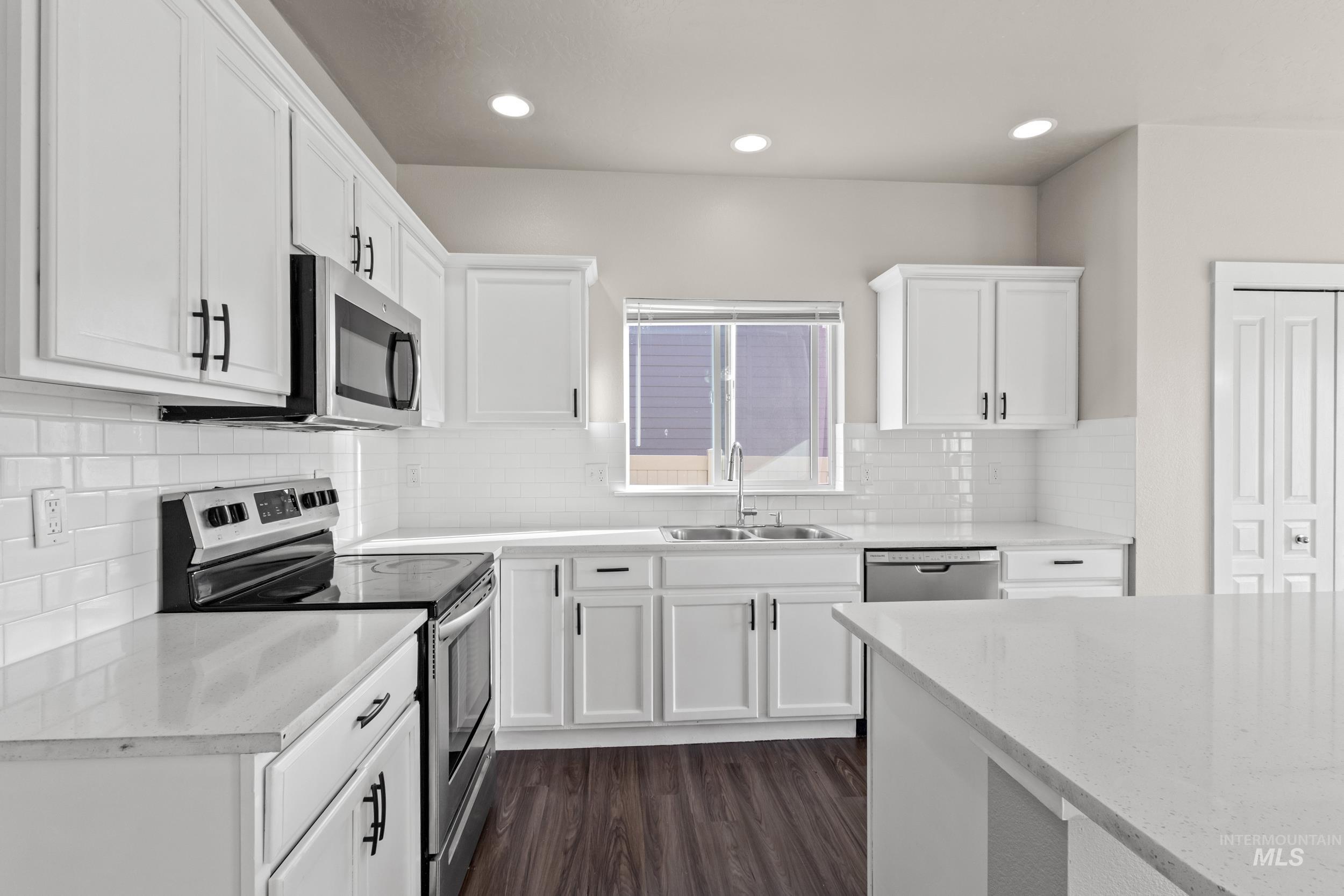 Kitchen featuring stainless steel appliances, white cabinets, dark wood finished floors, light stone counters, and recessed lighting