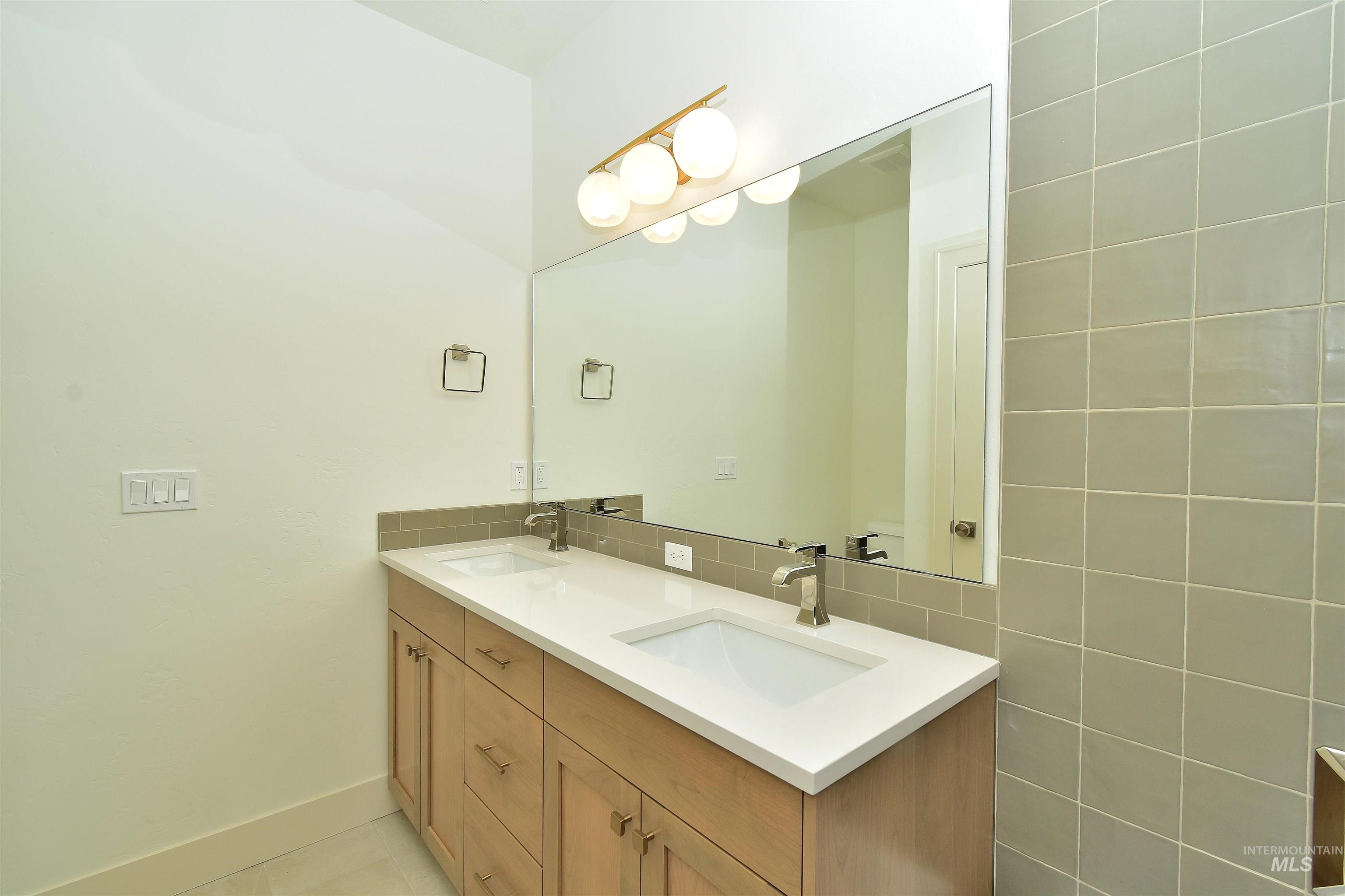 Bathroom with double vanity, decorative backsplash, and light tile patterned floors