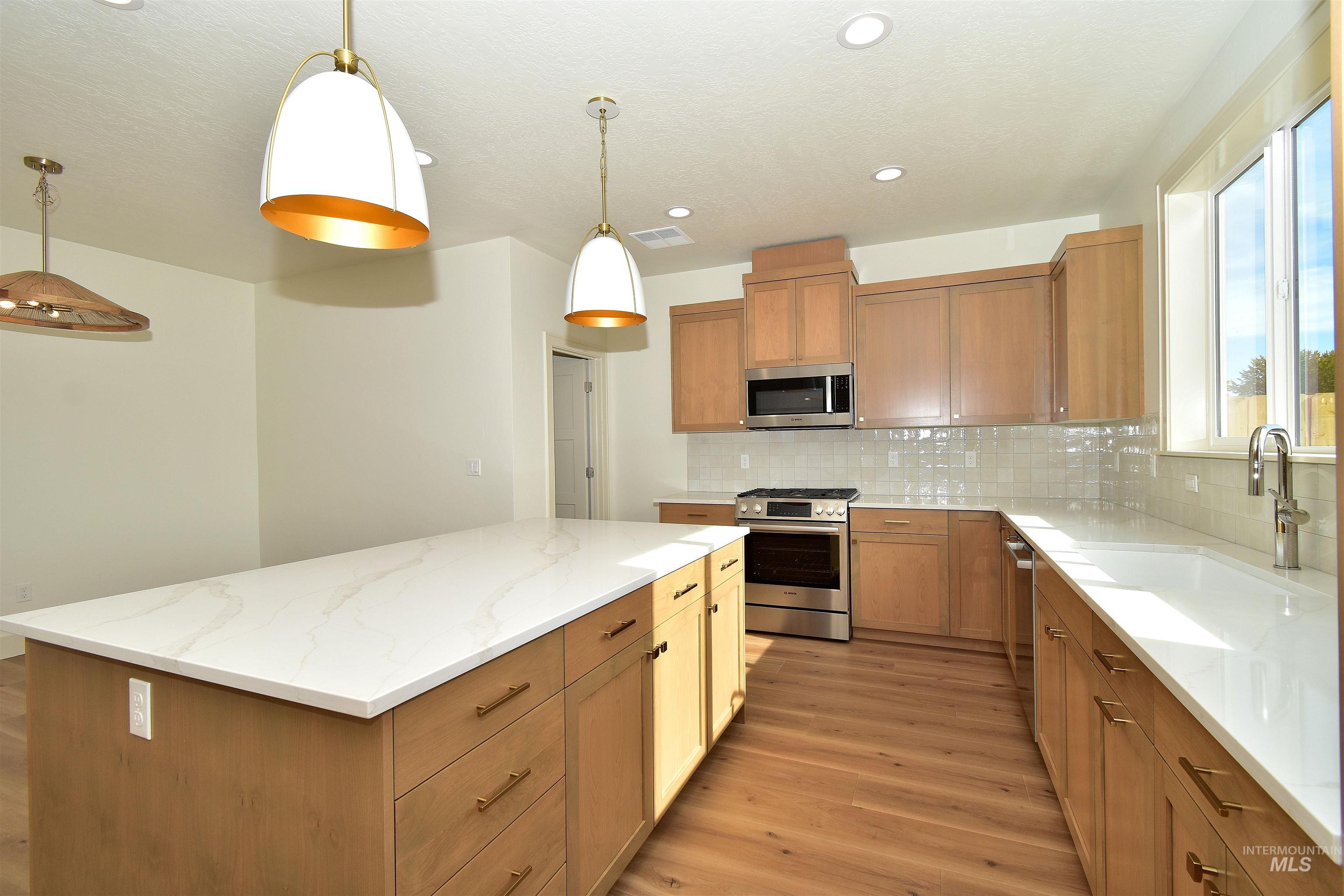 Kitchen with stainless steel appliances, light wood finished floors, light stone counters, a kitchen island, and decorative light fixtures
