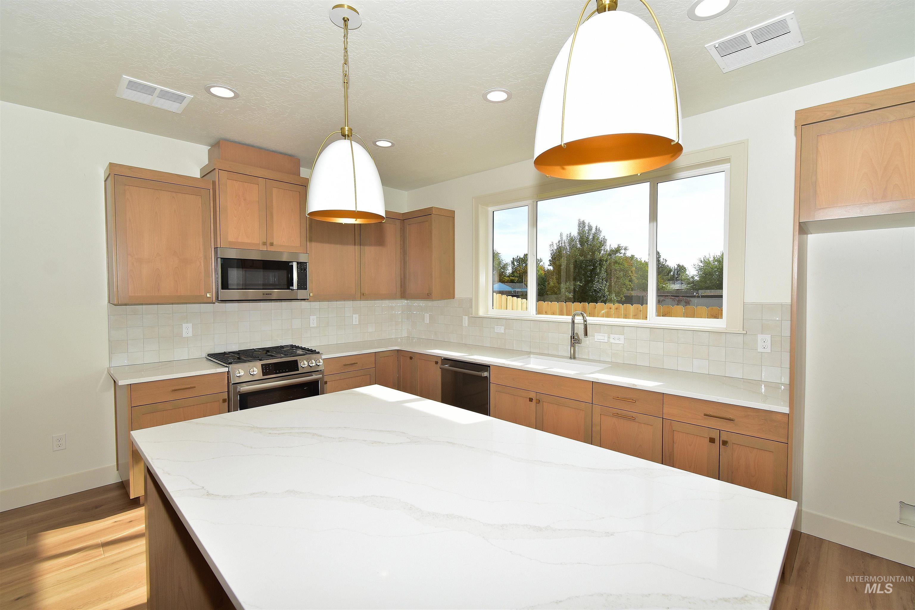 Kitchen with dark wood finished floors, light stone counters, decorative light fixtures, stainless steel appliances, and recessed lighting