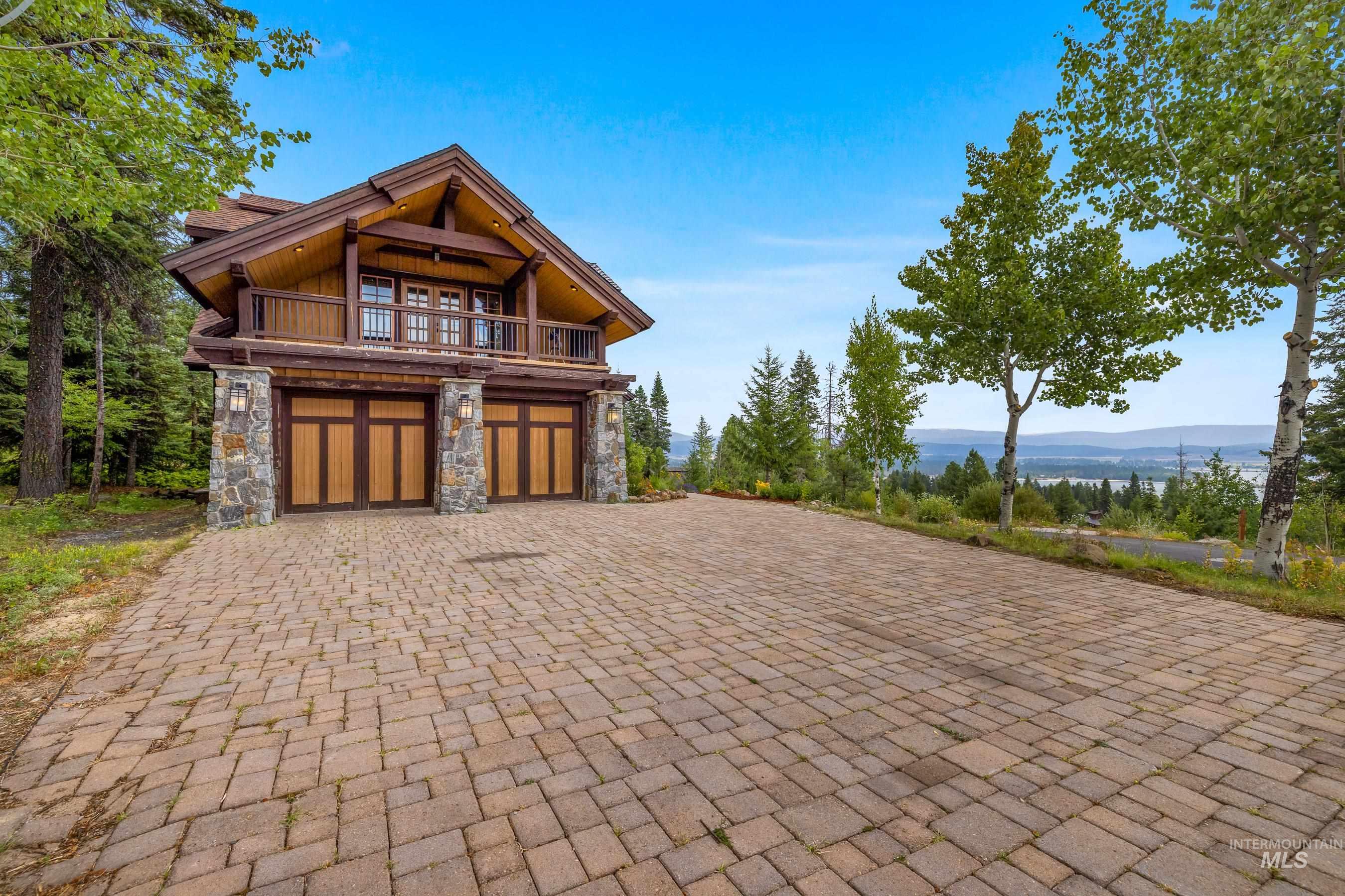 View of front of house featuring stone siding, decorative driveway, a mountain view, an attached garage, and a balcony