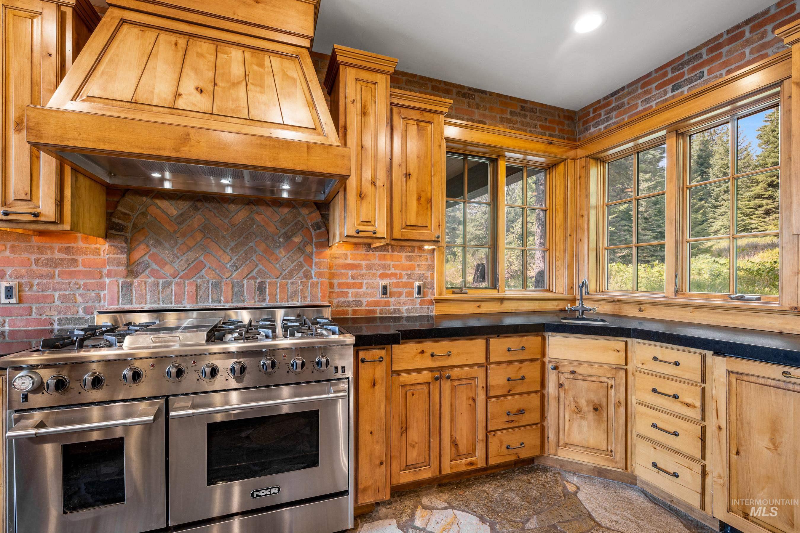 Kitchen featuring range with two ovens, custom exhaust hood, brick wall, brown cabinets, and granite tiled floors