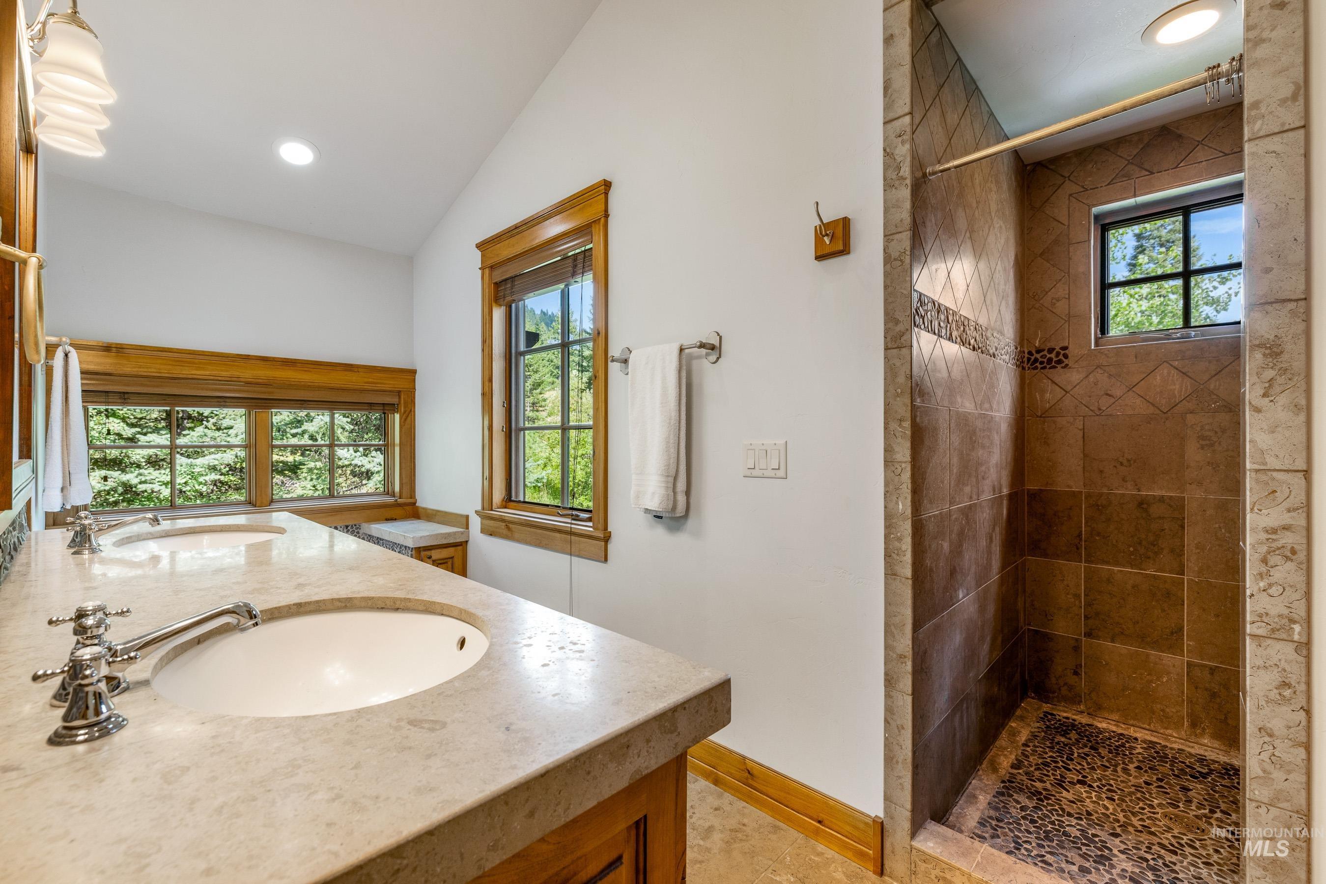 Full bath with a tile shower, double vanity, recessed lighting, and lofted ceiling