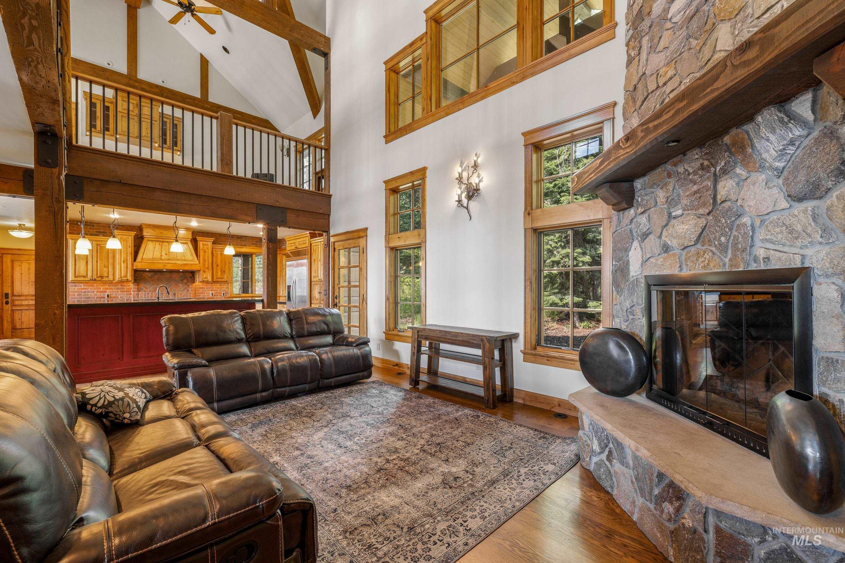 Living area with a stone fireplace, wood finished floors, a high ceiling, and a ceiling fan