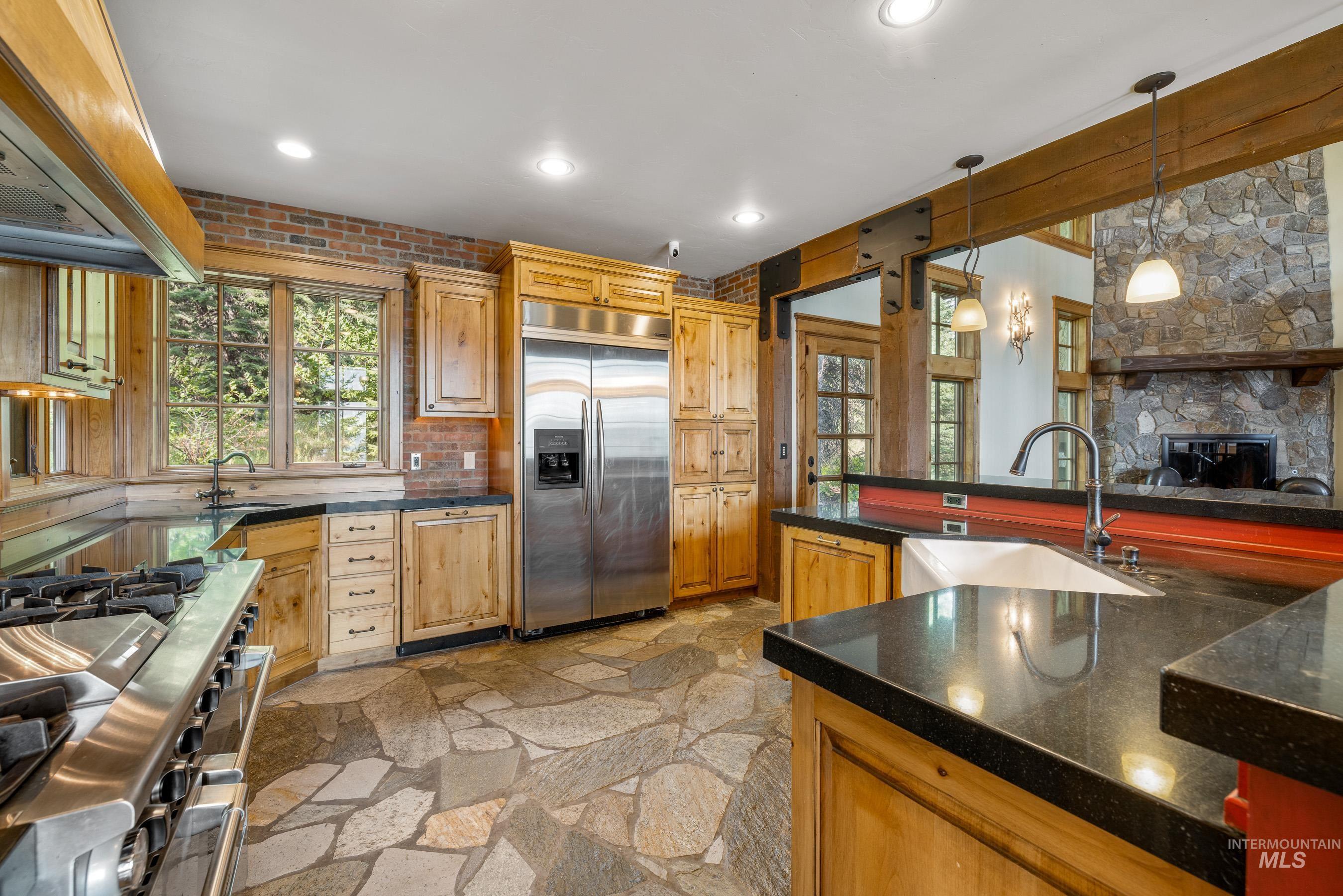 Kitchen with appliances with stainless steel finishes, custom range hood, pendant lighting, stone floors, and a fireplace