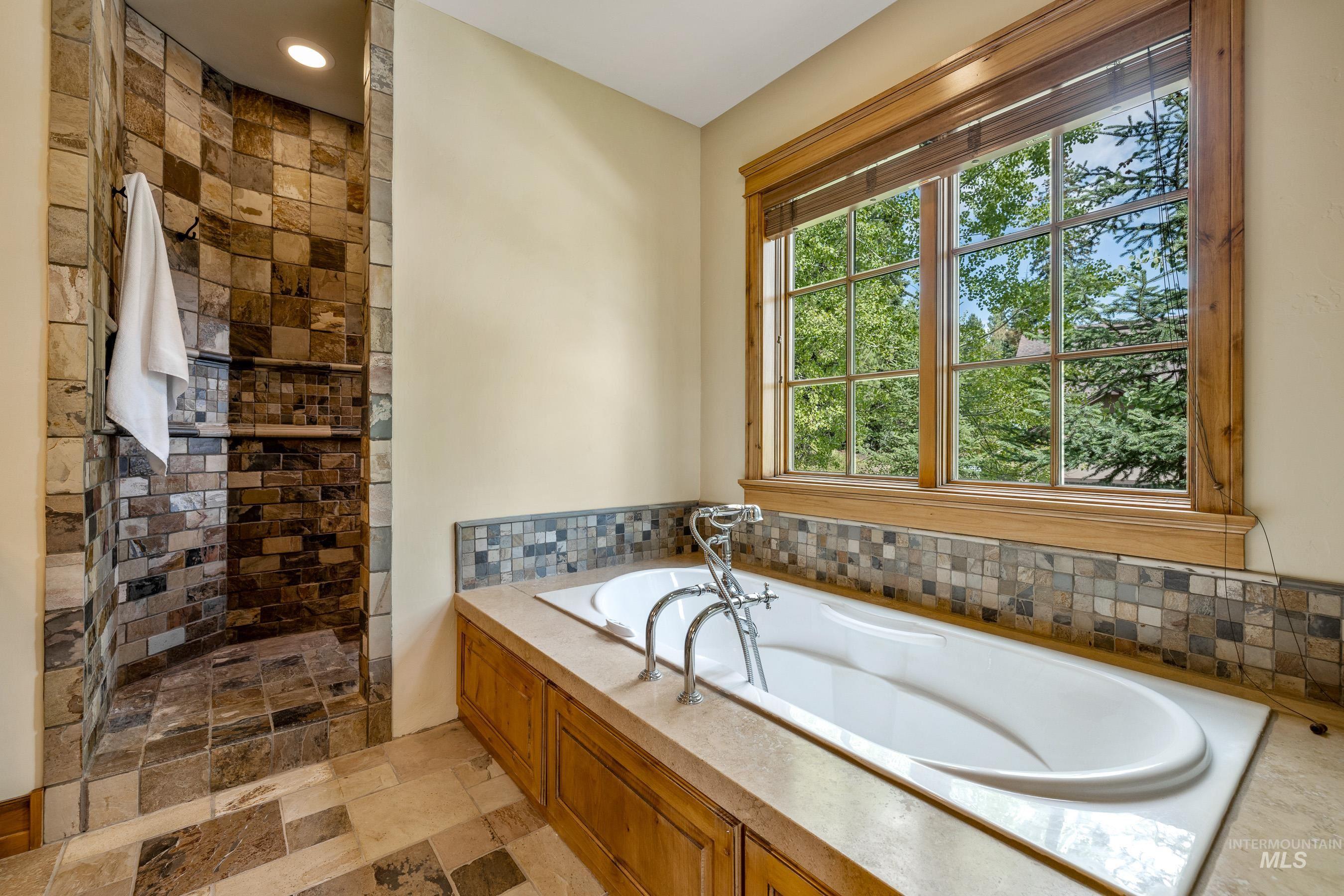 Bathroom featuring a bath, a walk in shower, and light stone finish flooring