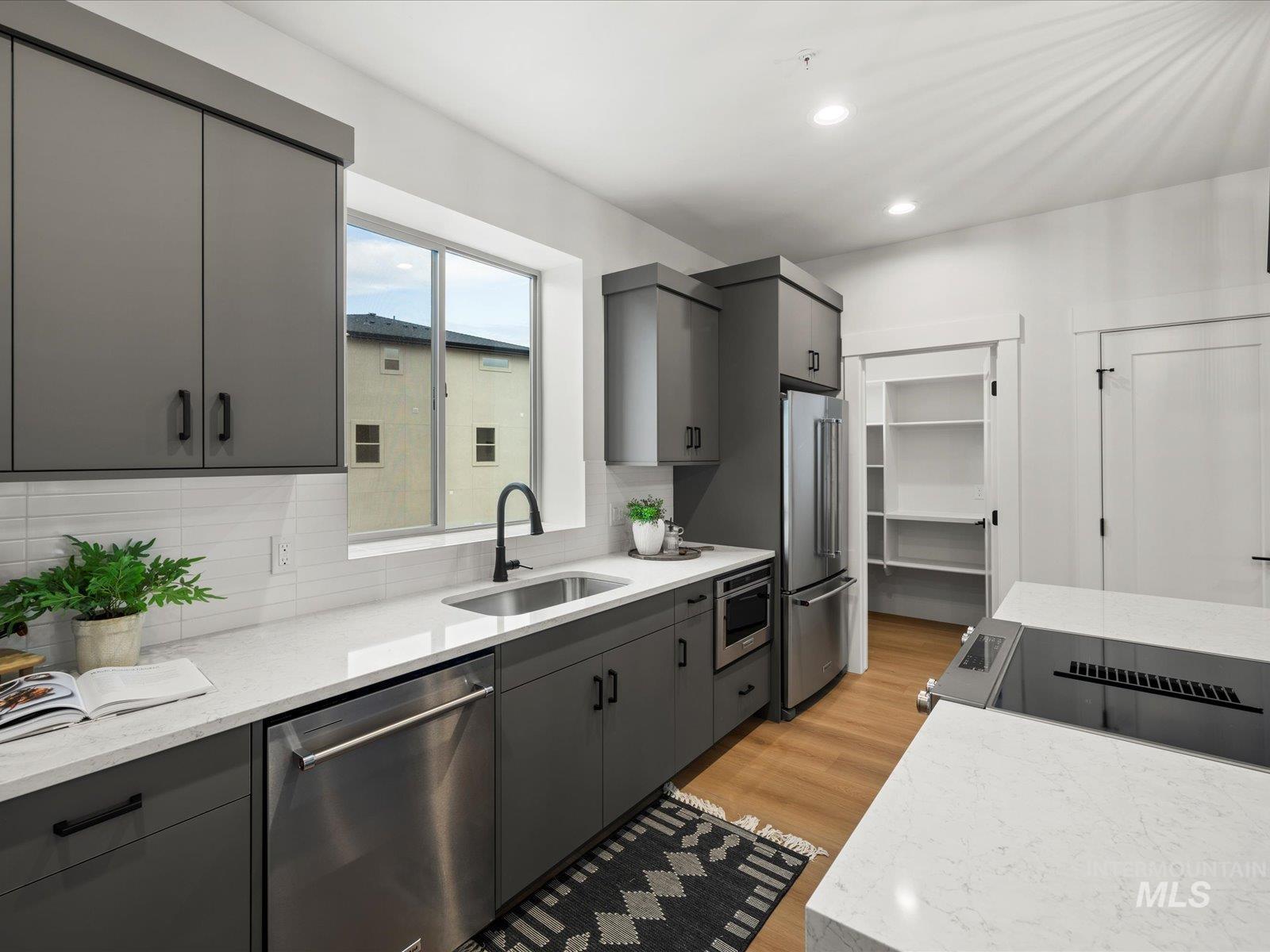 Kitchen with gray cabinetry, appliances with stainless steel finishes, light wood-style flooring, light stone countertops, and tasteful backsplash