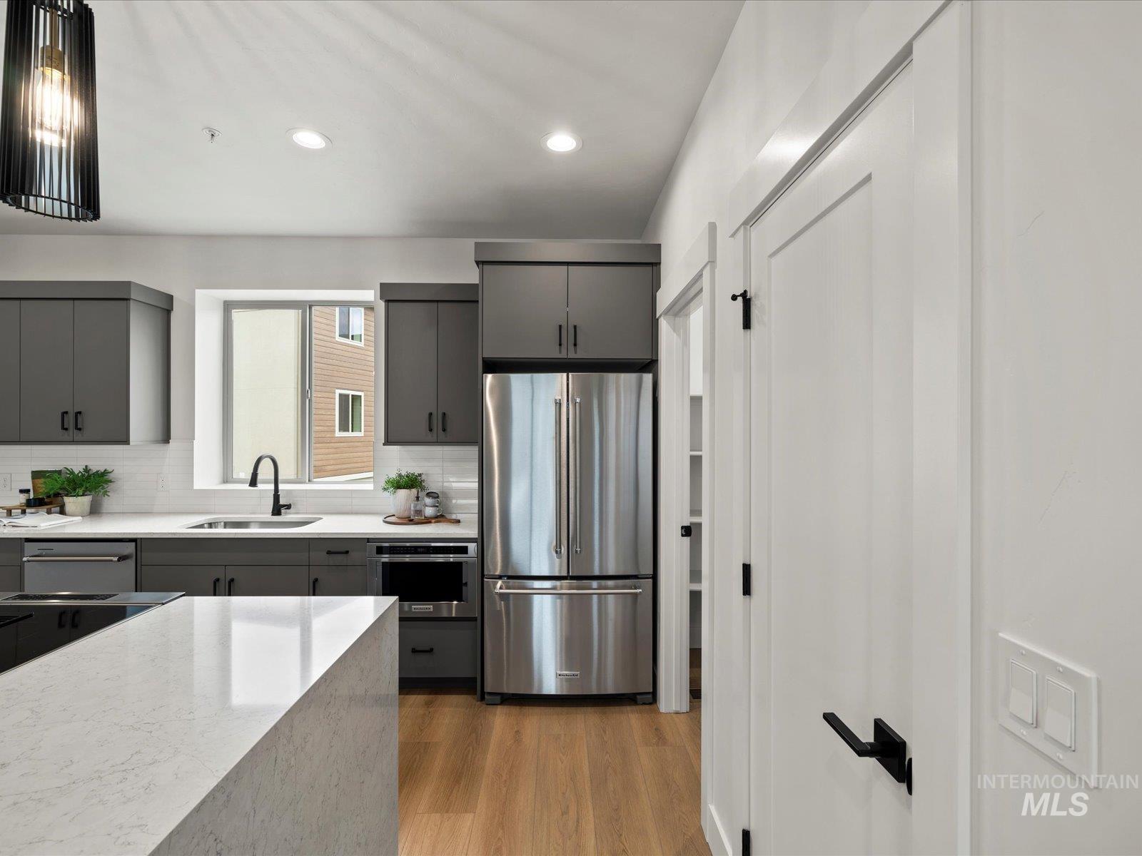 Kitchen with appliances with stainless steel finishes, recessed lighting, light wood finished floors, decorative backsplash, and gray cabinetry
