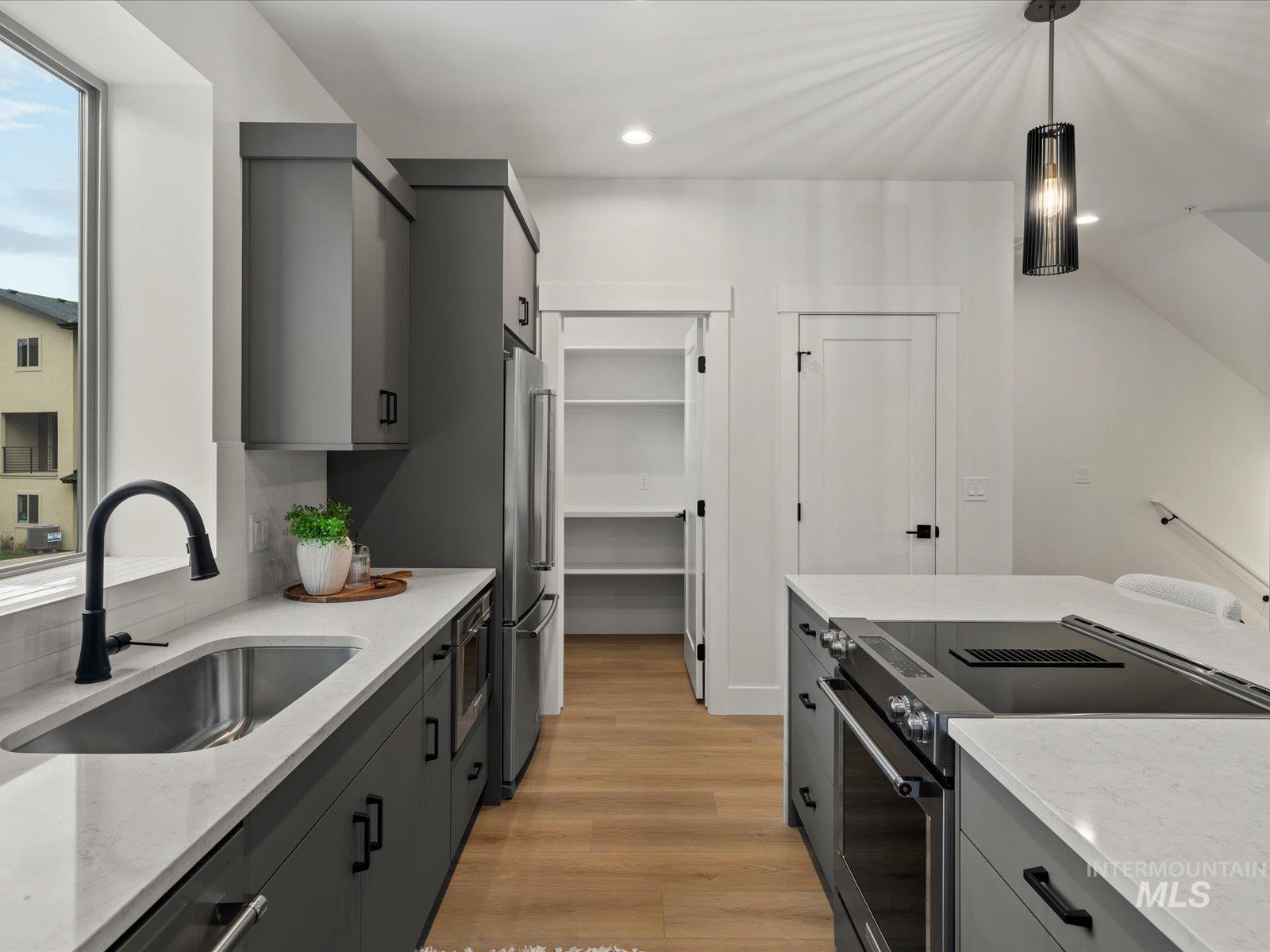 Kitchen with gray cabinets, stainless steel appliances, light wood-style flooring, light stone countertops, and decorative light fixtures