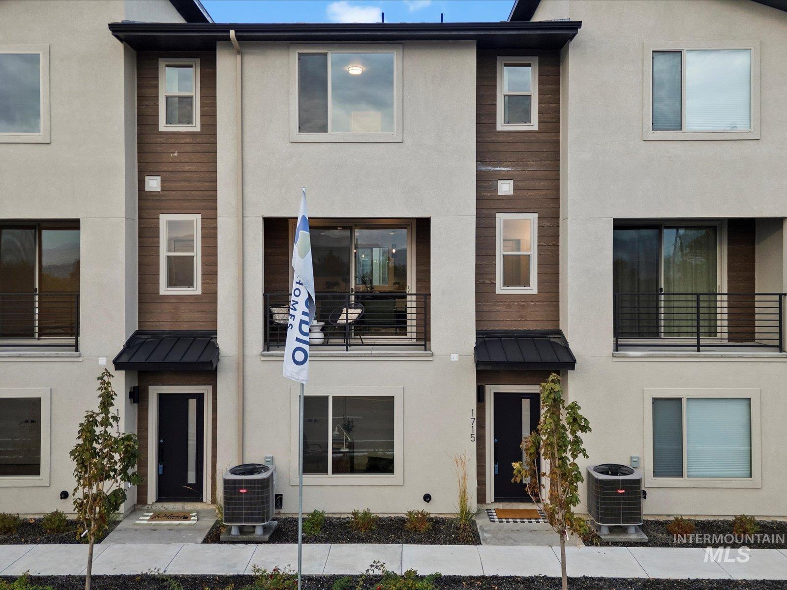 View of front of house featuring a standing seam roof, a metal roof, stucco siding, and a balcony