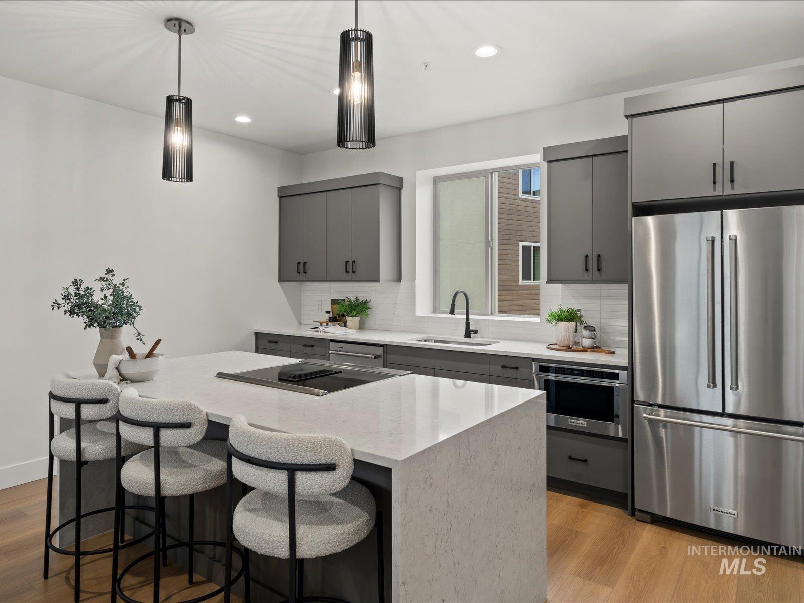 Kitchen featuring gray cabinets, stainless steel appliances, a breakfast bar, pendant lighting, and light wood-type flooring